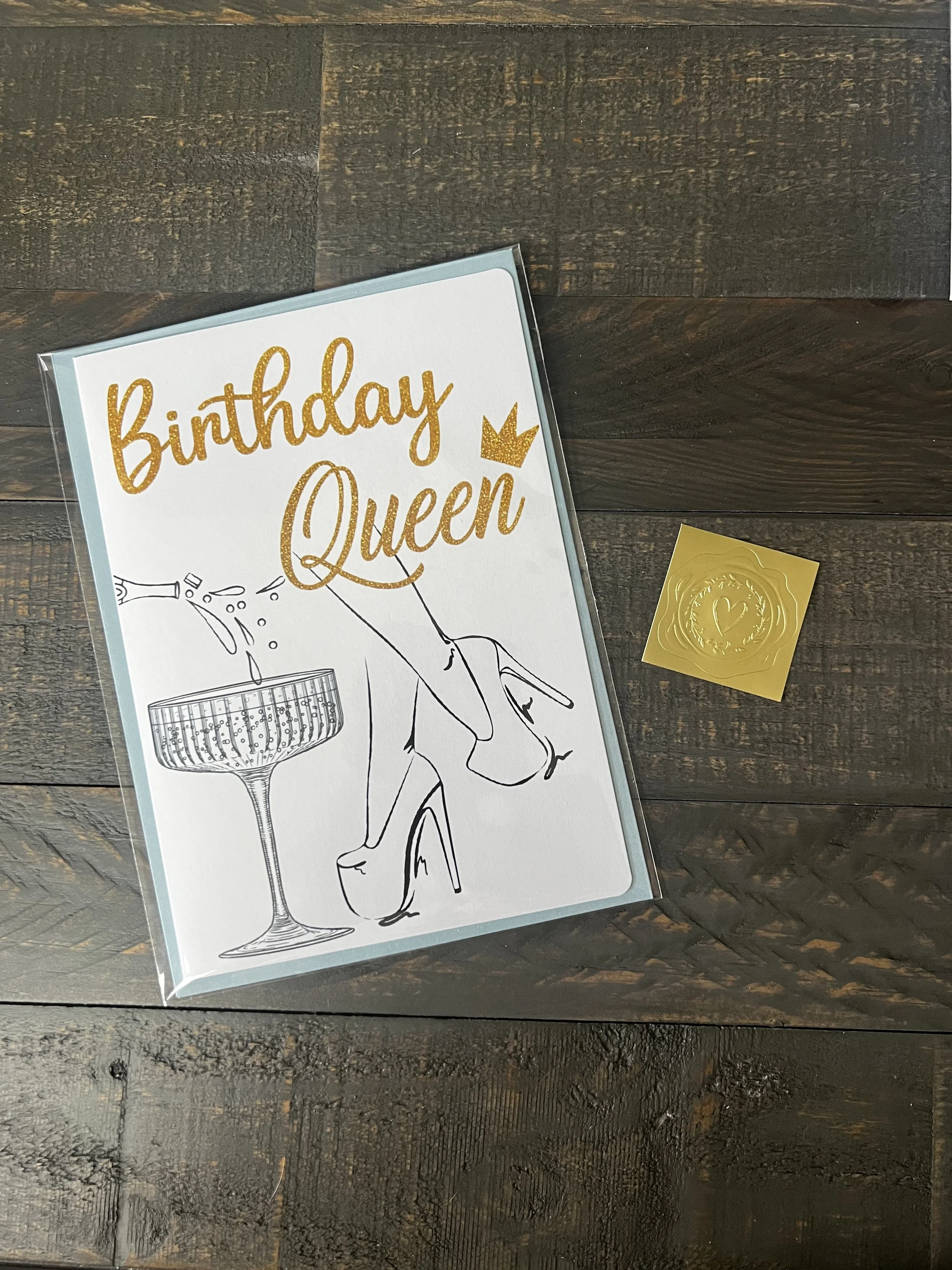 Styled flat lay of Birthday Queen greeting card with coordinating envelope and gold wax seal style sticker.
