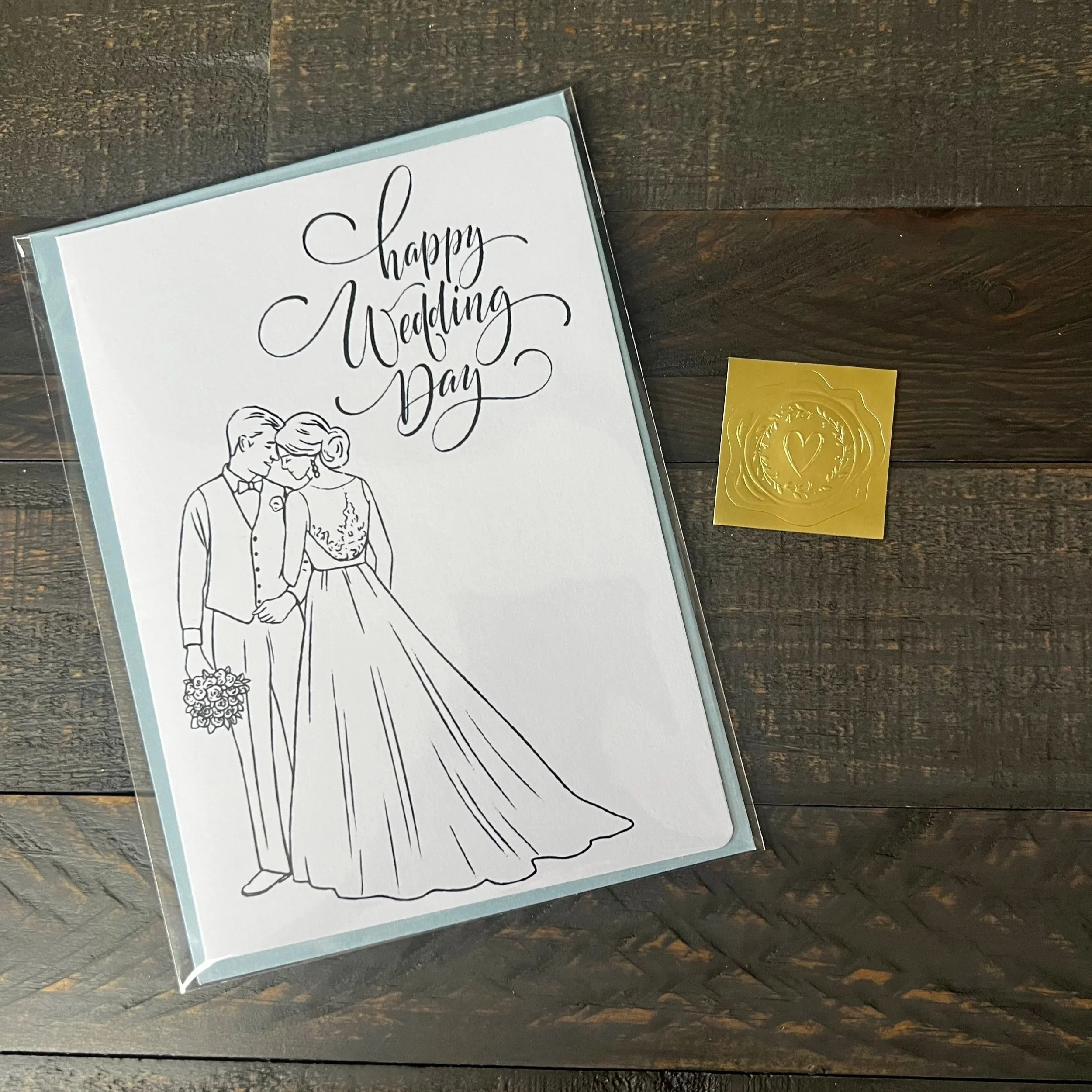 Styled flat lay of Happy Wedding Day Card with coordinating soft blue envelope and gold wax seal style sticker.