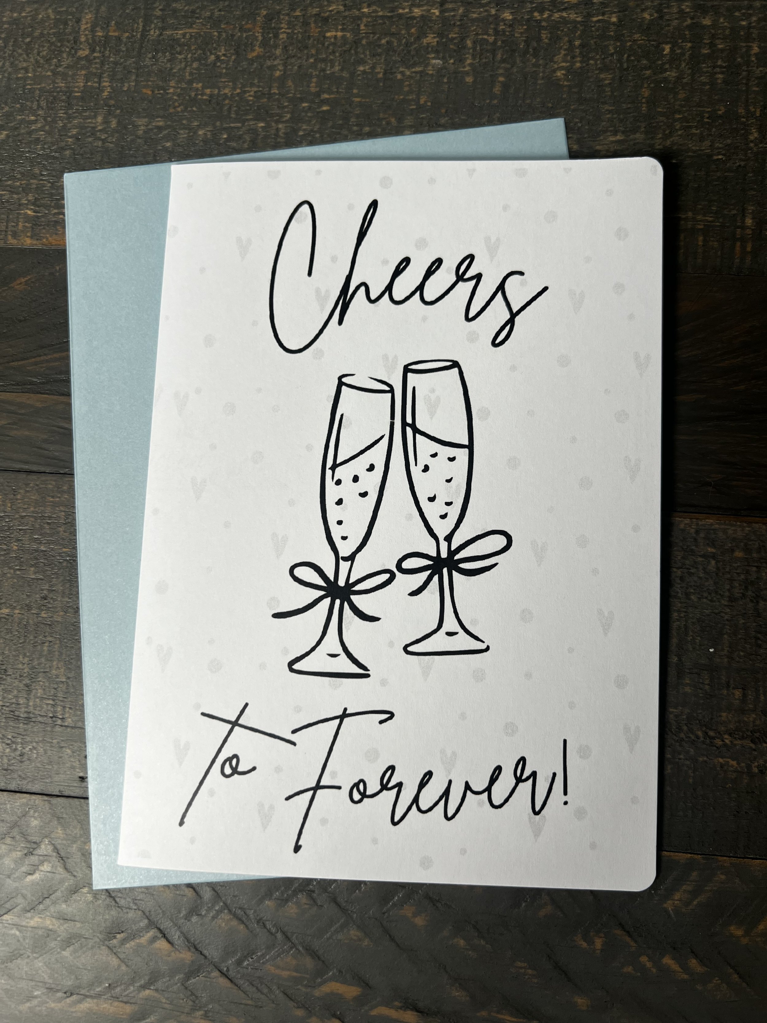 Front of Cheers to Forever engagement card with coordinating soft blue envelope.