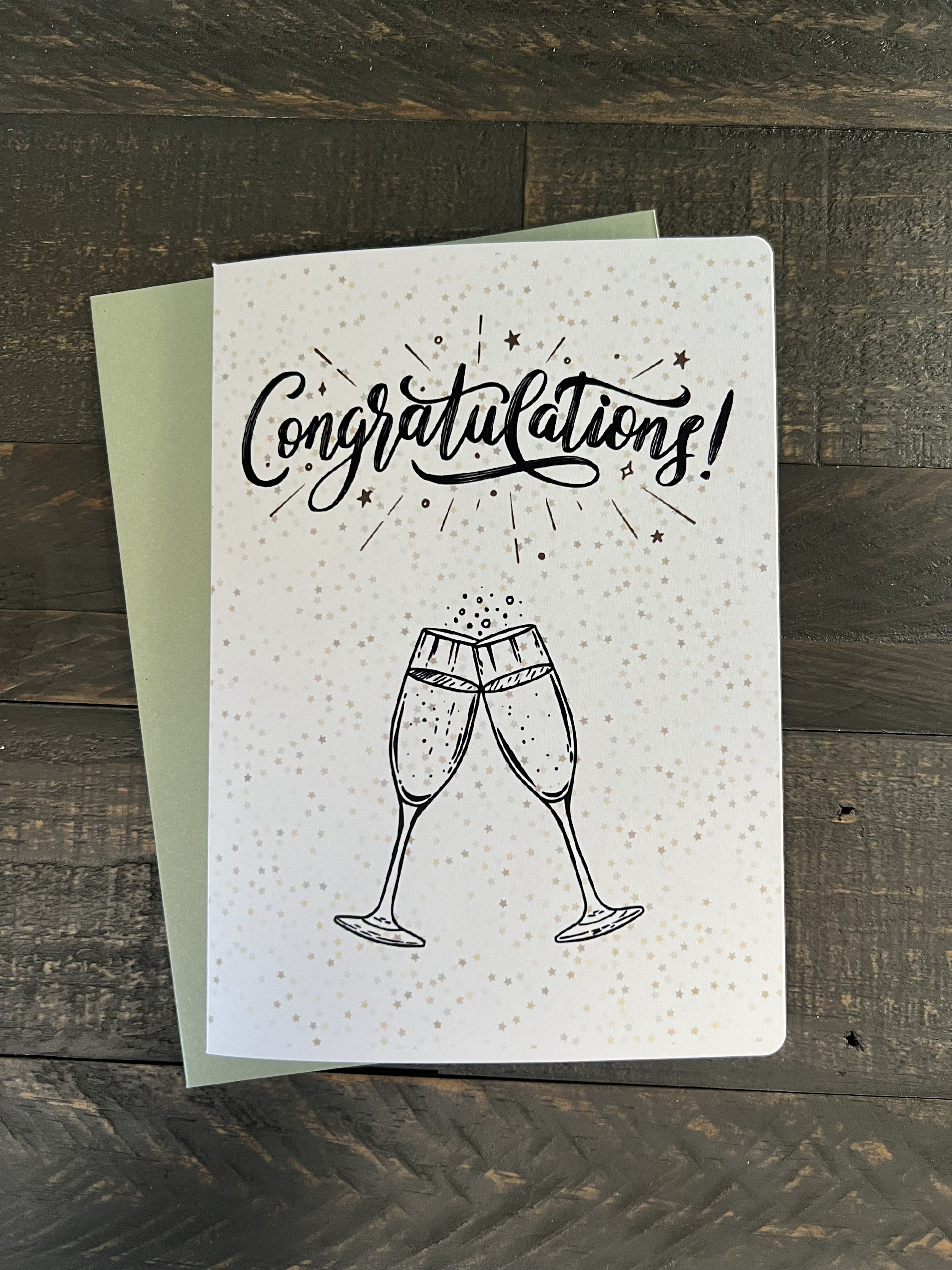 Congratulations greeting card with champagne glasses illustration and gold speckled design on wood background