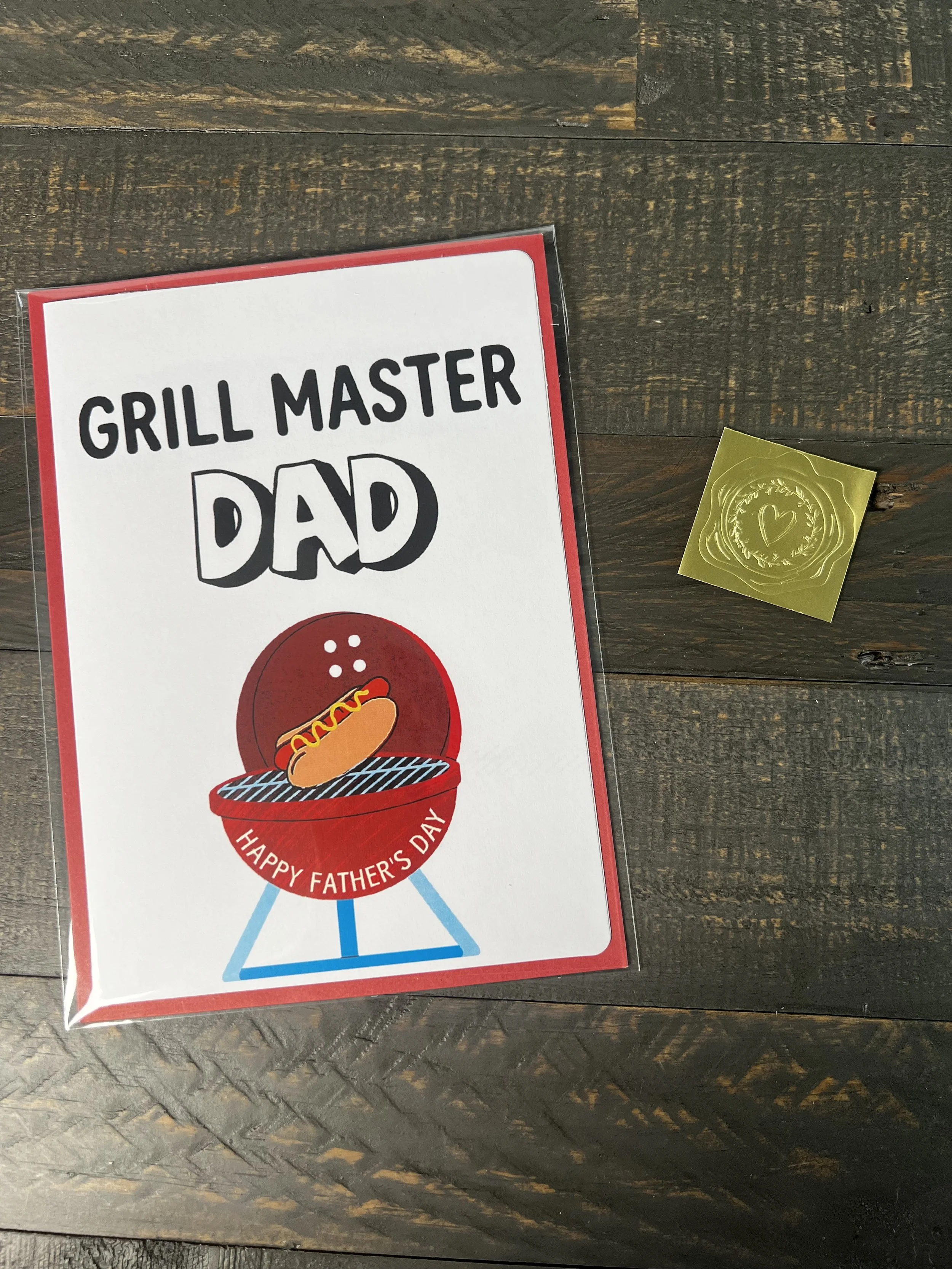 BBQ Father’s Day card styled with coordinating red envelope and gold wax seal sticker on wood background