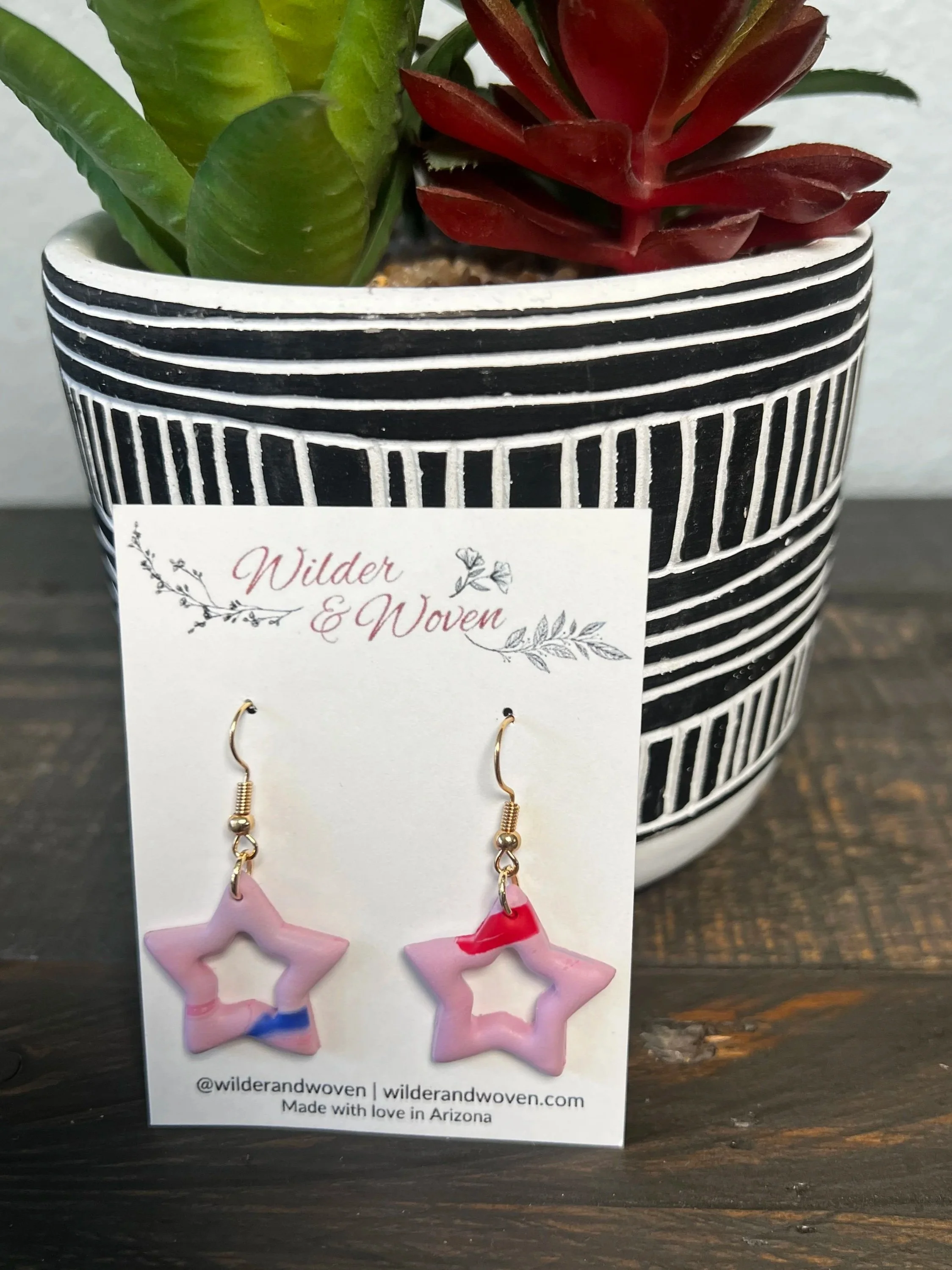 Handmade blush pink marbled polymer clay open star earrings with patriotic accents hanging from gold fishhook ear wires.
