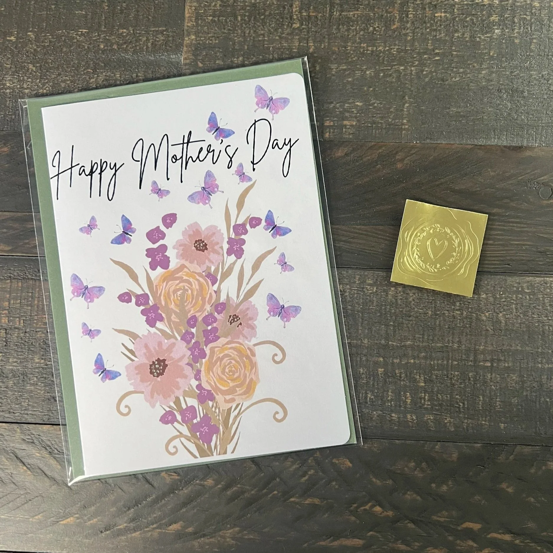 Packaged Mother’s Day card with butterfly bouquet design, sage green envelope, and gold wax seal sticker on wood surface