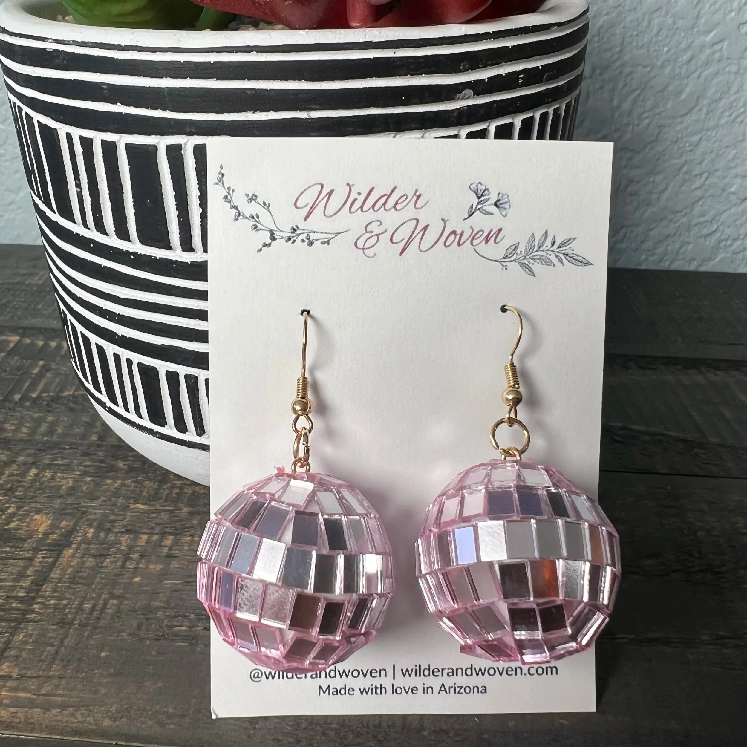 Light pink mirrored disco ball charm earrings displayed on a Wilder & Woven branded jewelry card.