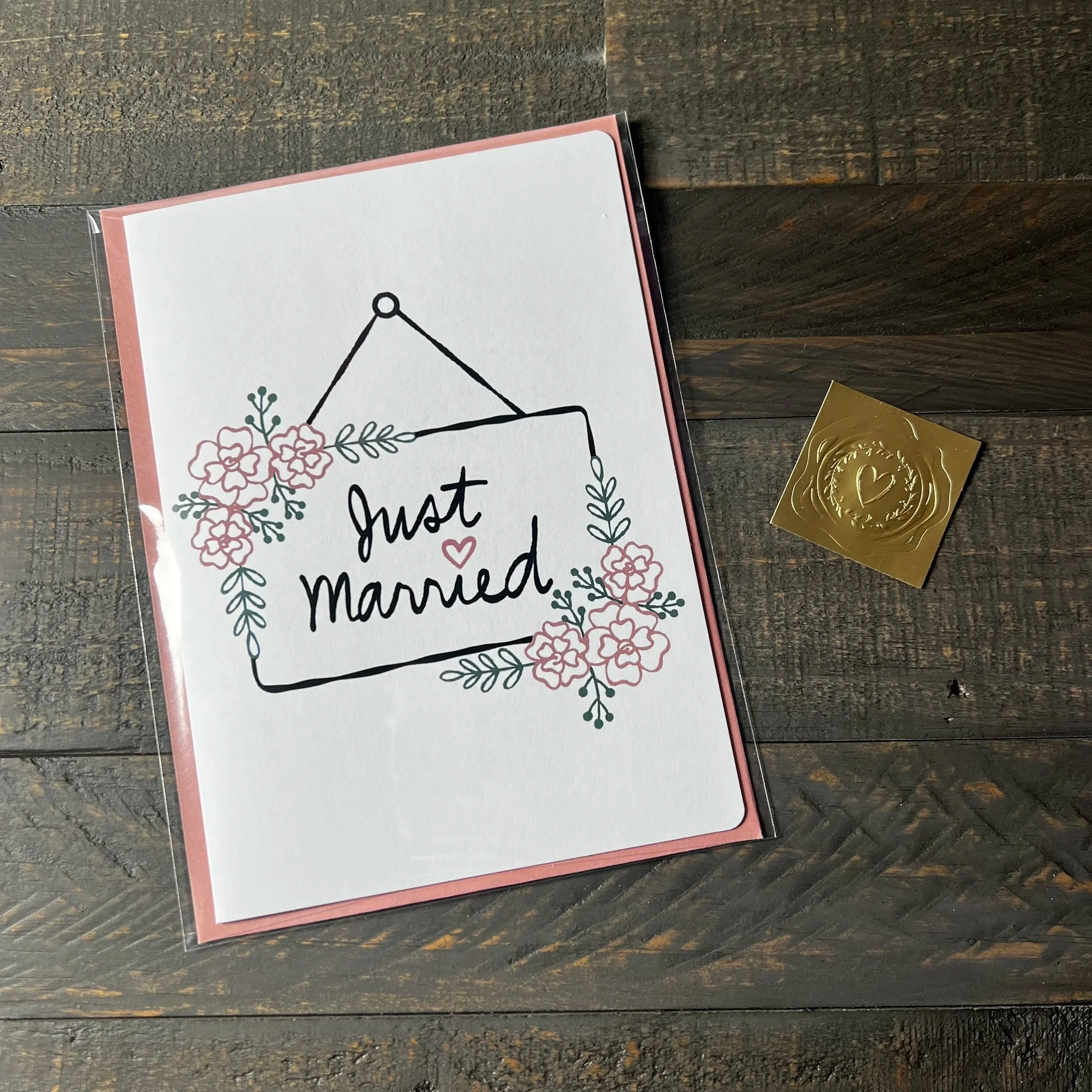 Styled flat lay of Just Married Wedding Card with coordinating blush pink envelope and gold wax seal style sticker.
