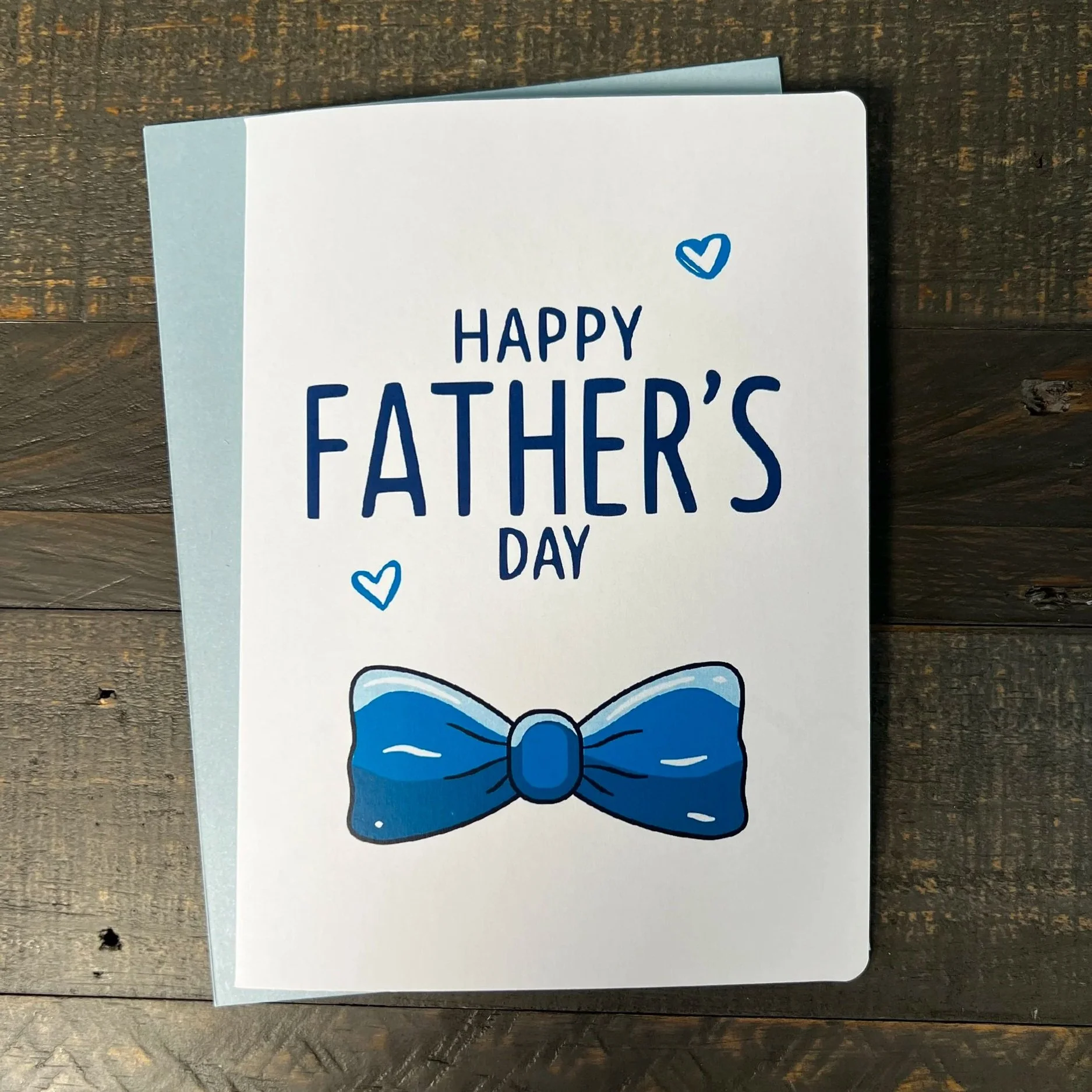 Father’s Day card with blue bow tie design and modern typography on wood background
