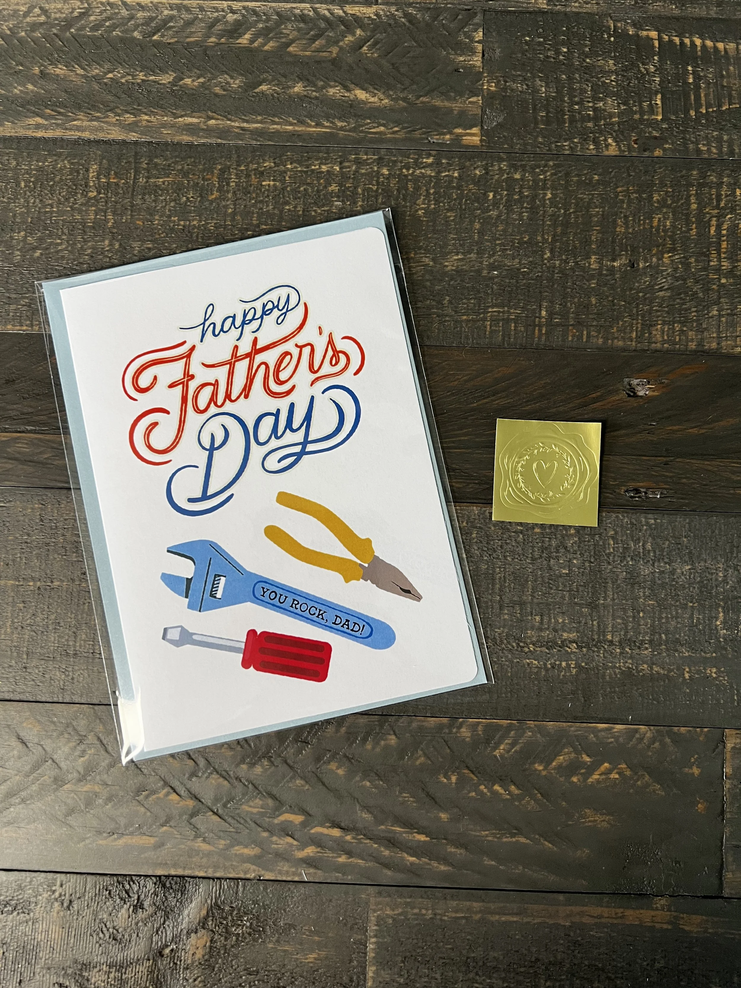 Father’s Day card styled with light blue envelope and gold wax seal sticker on wood background