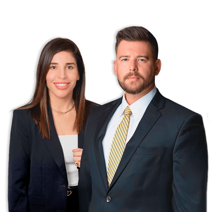 Two professionally dressed individuals, a woman and a man, posing against a black background. The woman has long brown hair and is smiling, while the man has short hair, a beard, and is looking serious.