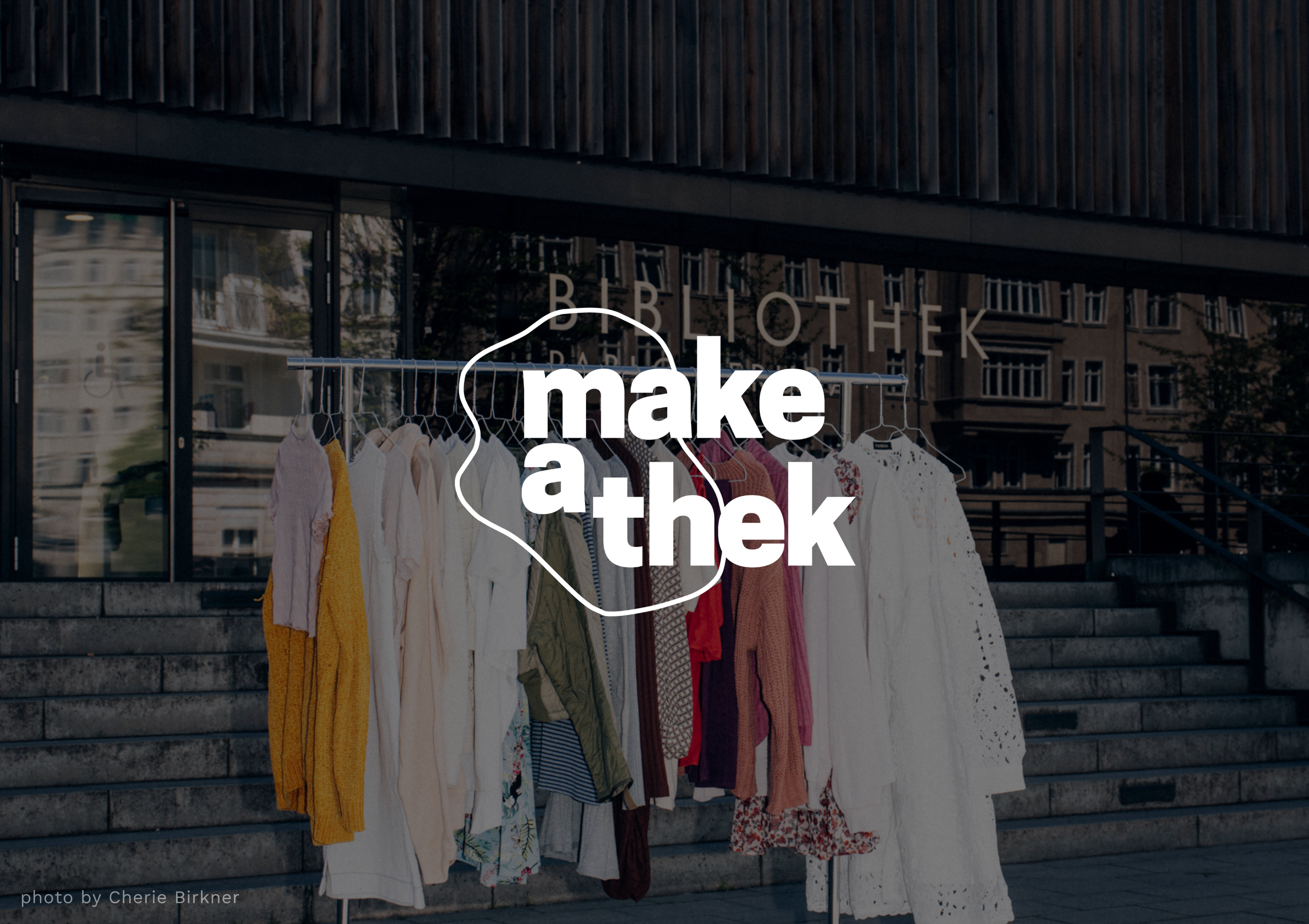 Logo of make-a-thek on a photograph of clothes rack infront of a library