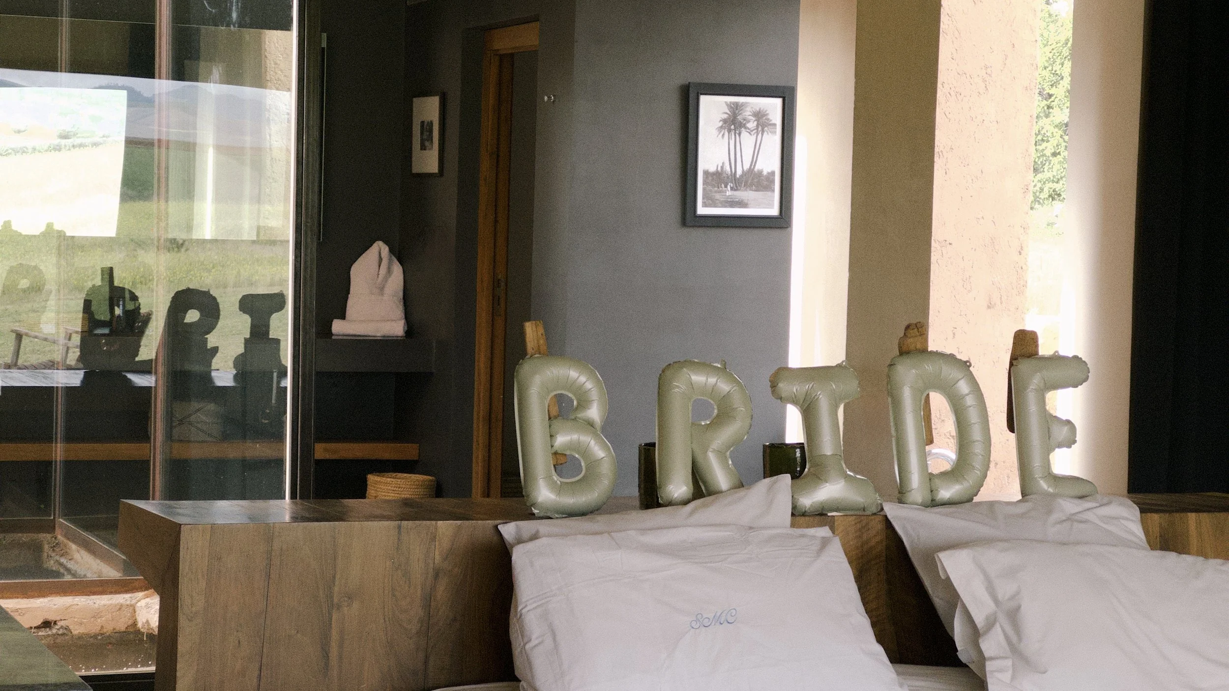 Decorative balloons spelling 'BRIDE' on a bed with white pillows in a room with framed pictures and large windows. Bachelorette trip morocco.