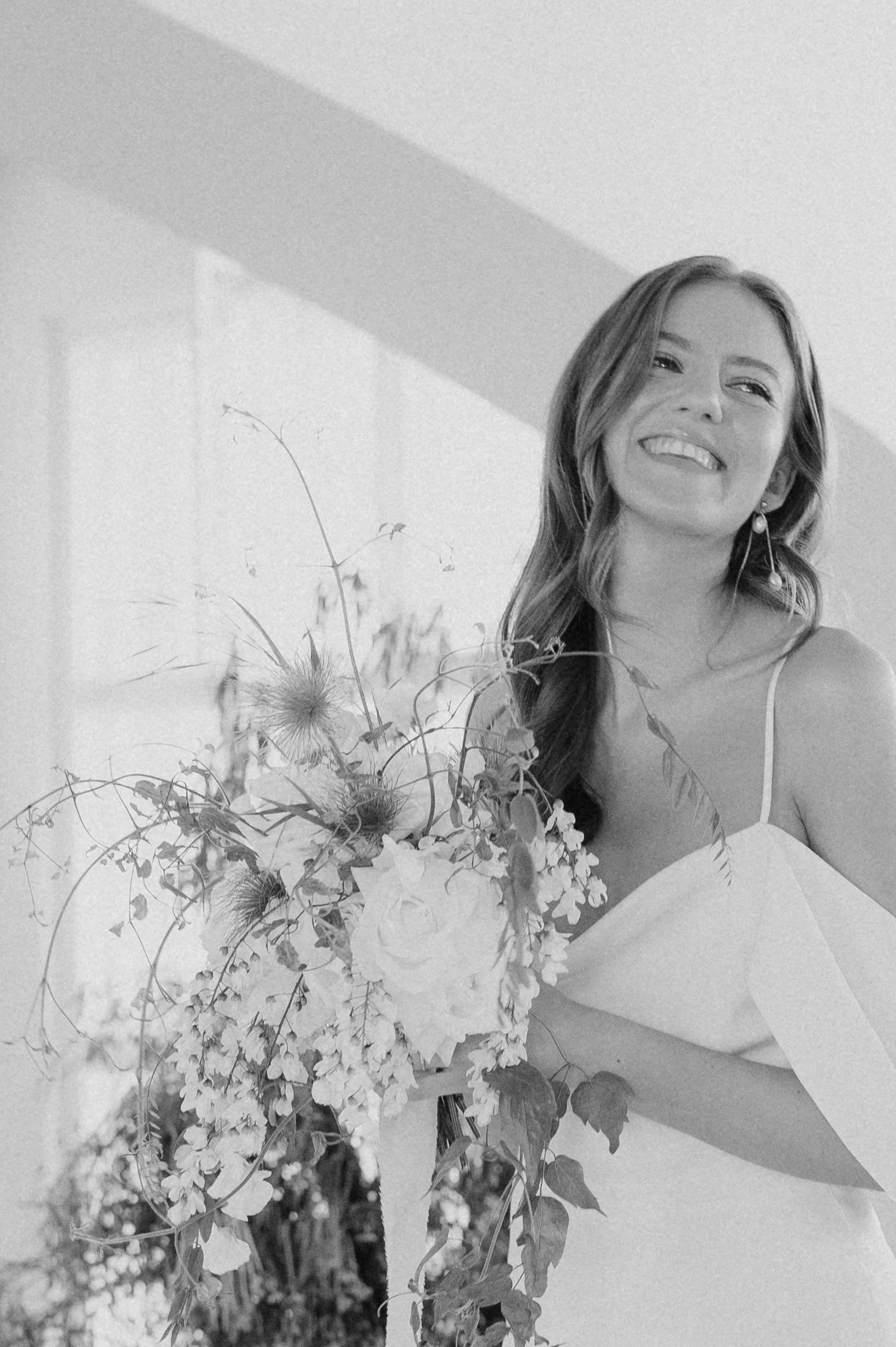 Eine lachende junge Frau in einem weißen Kleid hält einen großen Blumenstrauß.