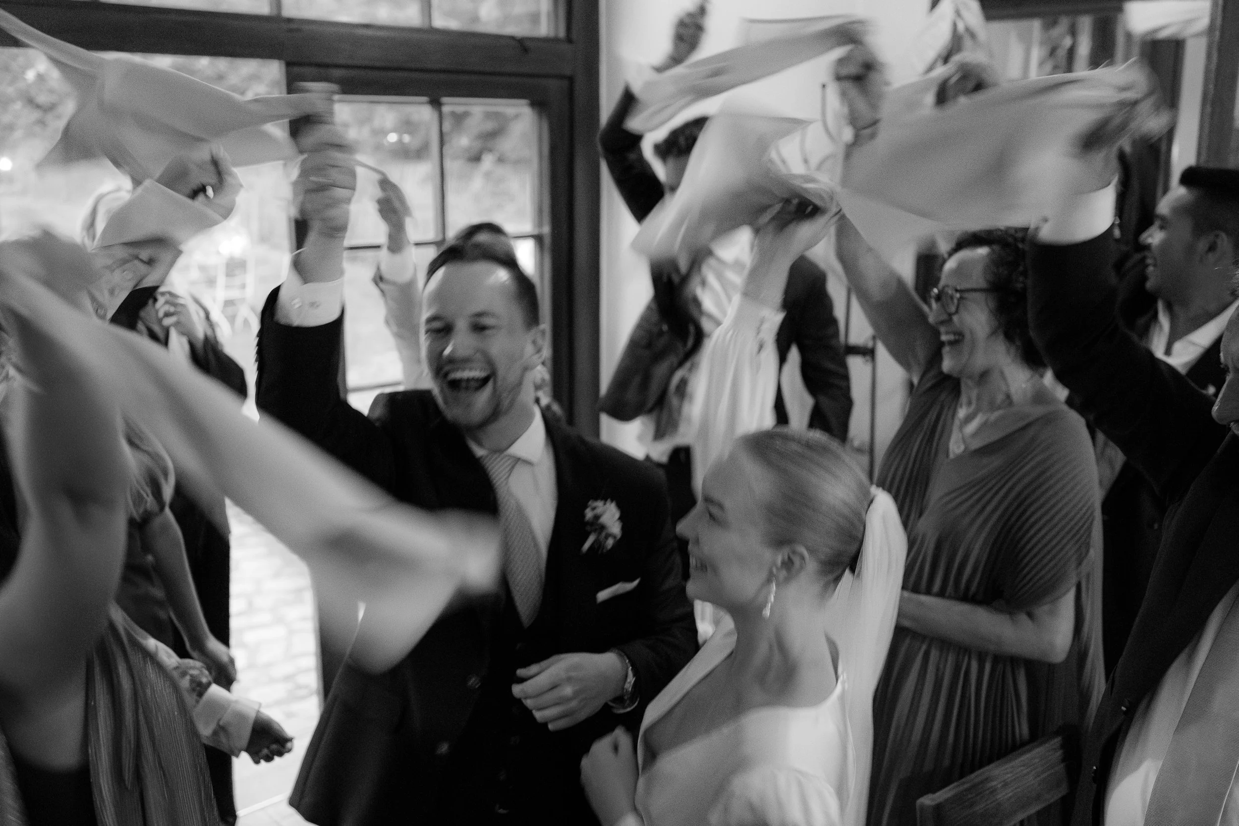 Menschen feiern mit Tüchern in einem festlichen Raum, lachen und umarmen sich, eine Hochzeitsgesellschaft.