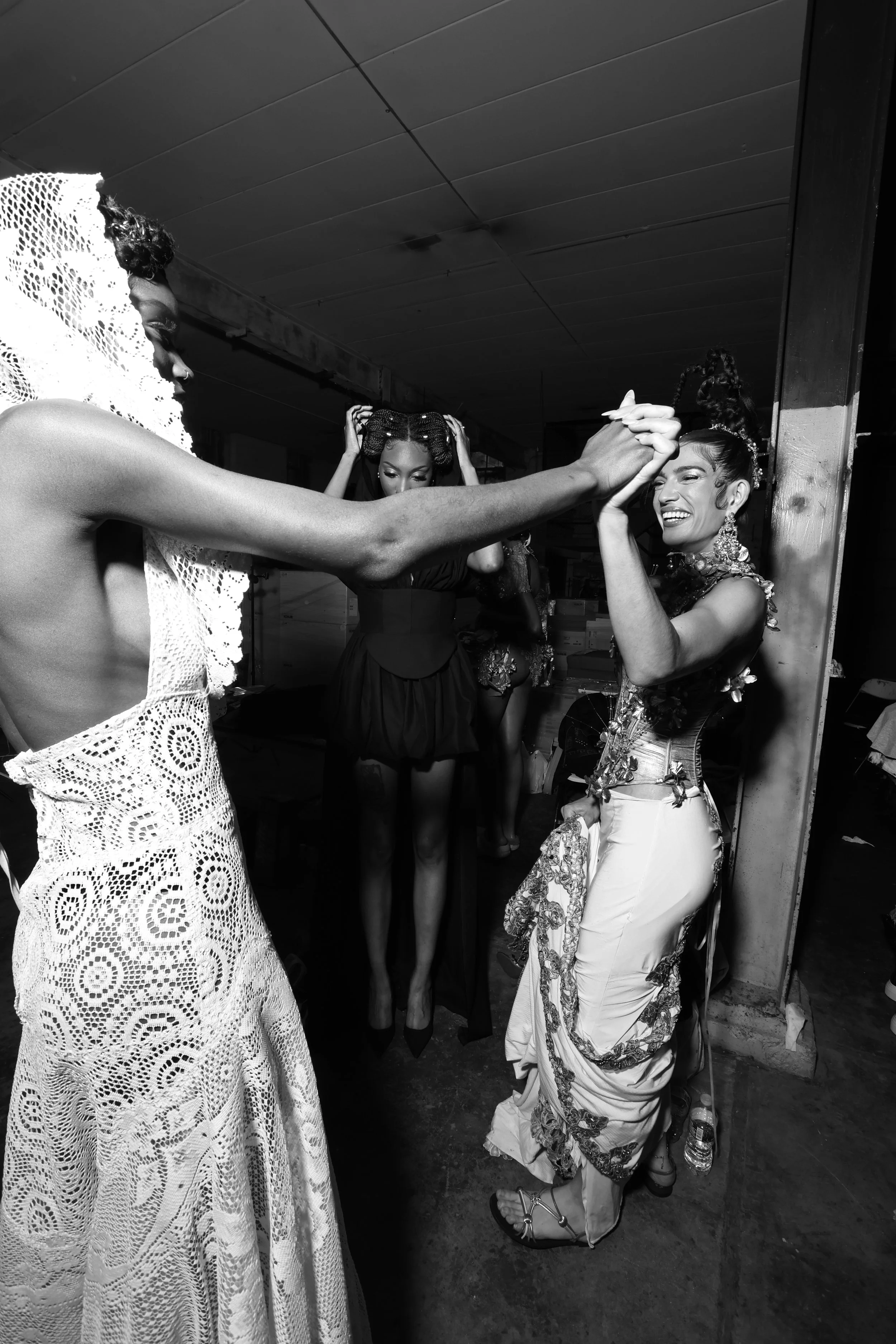 Women dancing and celebrating in a lively setting, with one woman in ornate attire smiling and others dressed in fashionable outfits.