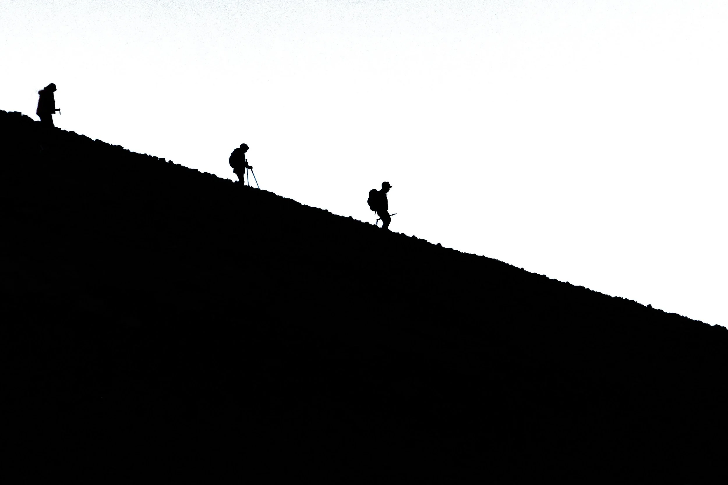 Silhouettes of four hikers climbing a hillside at sunset or sunrise.
