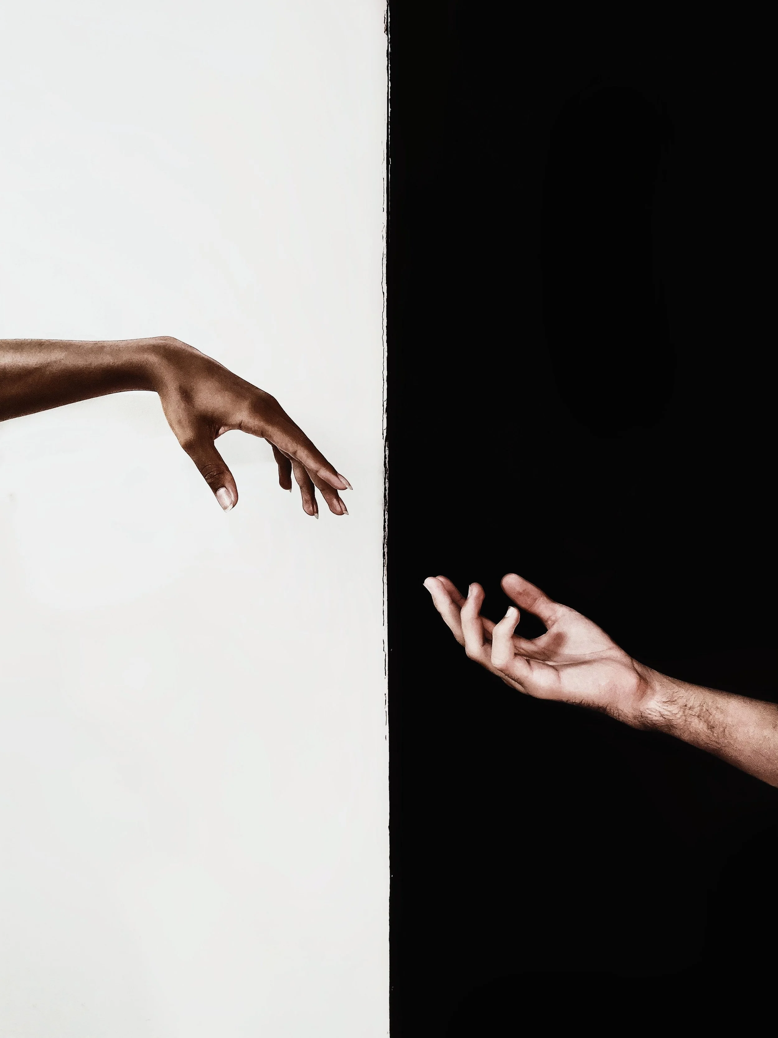 Photo of two hands reaching towards each other, separated by a vertical line dividing a black and white background.