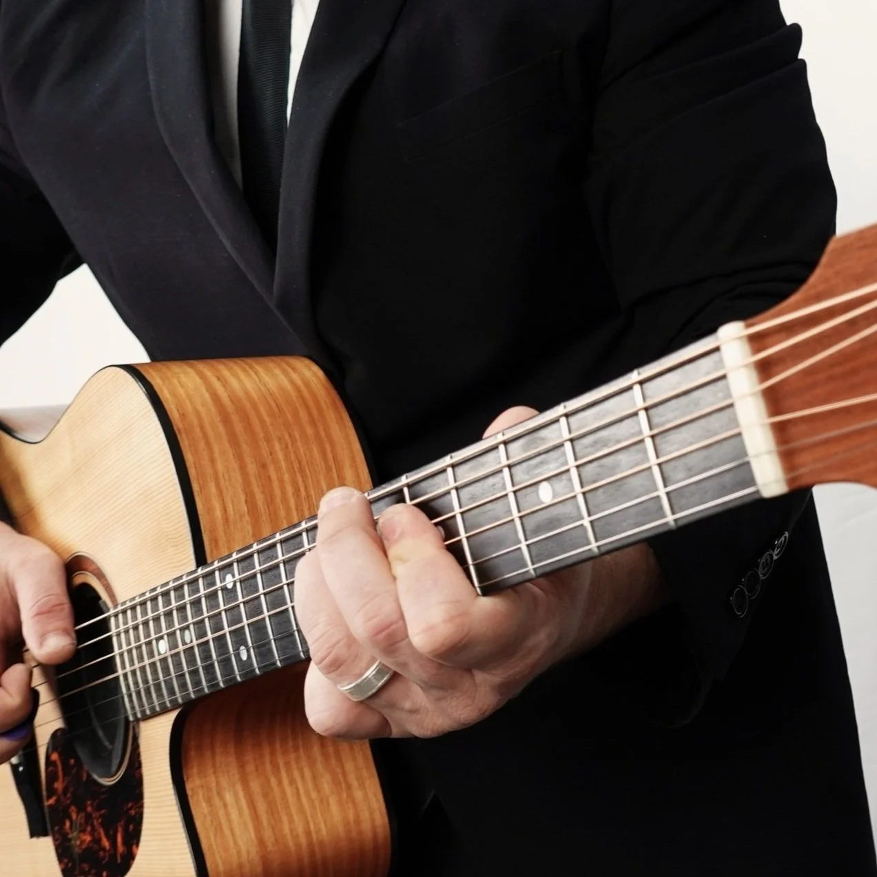 In Adelaide, Jasper C Music person in a black suit playing an acoustic guitar.