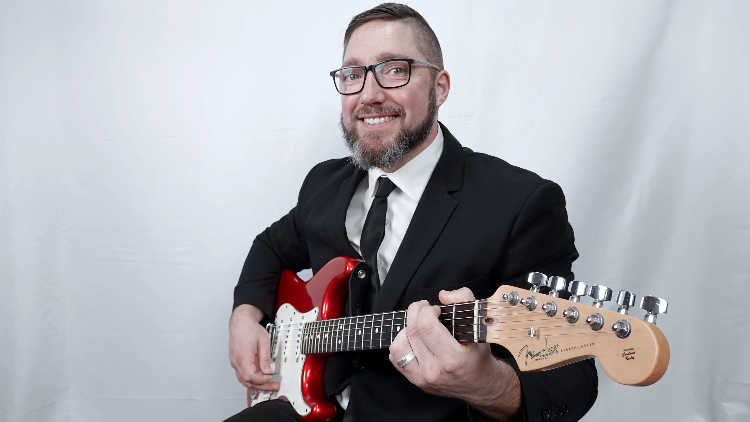 Adelaide musician, Jasper C Music with  guitar, sitting in music studio with white background.