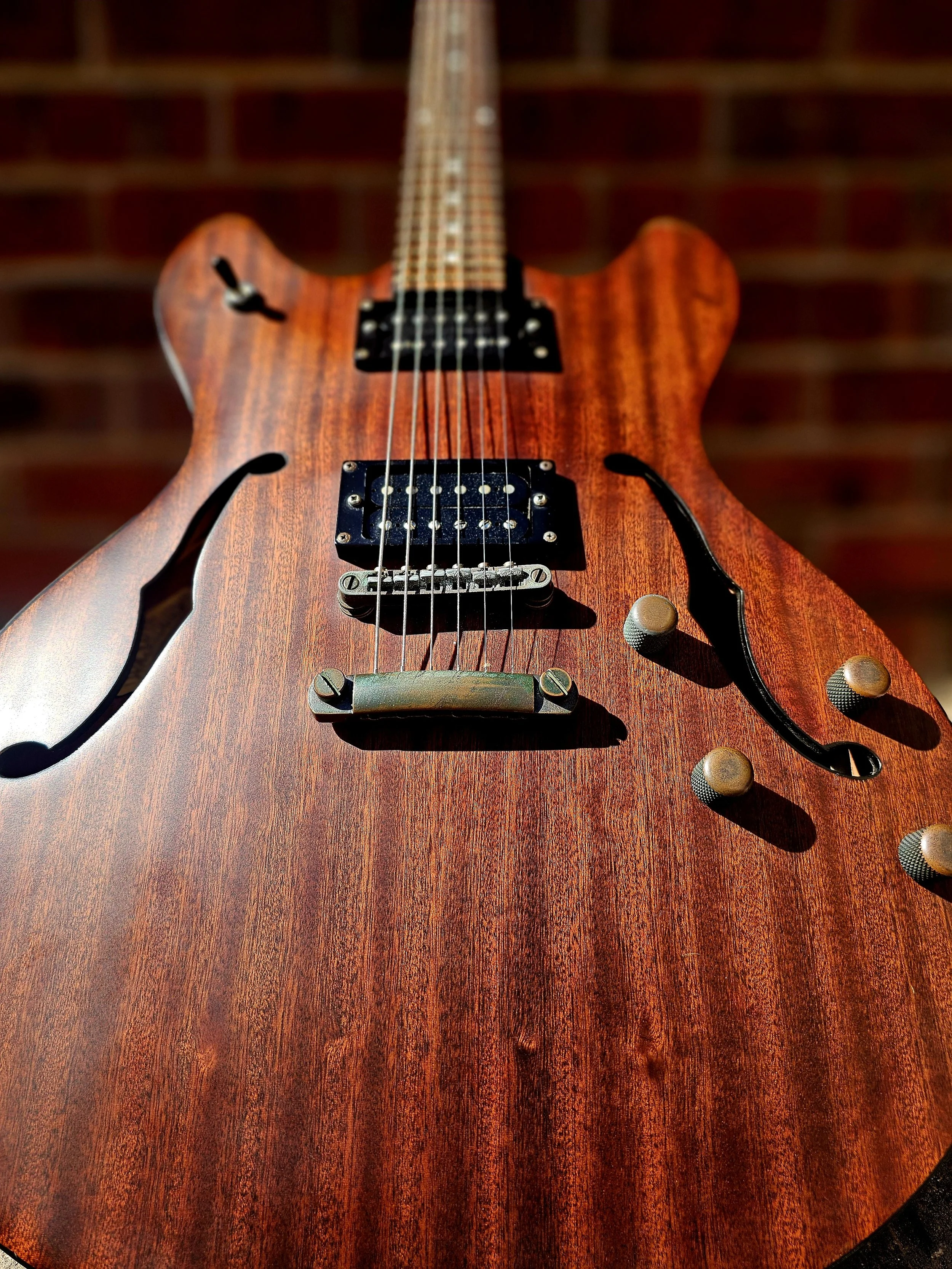 Close-up of a semi-hollow electric guitar with a wooden finish and visible strings, pickups, and control knobs.