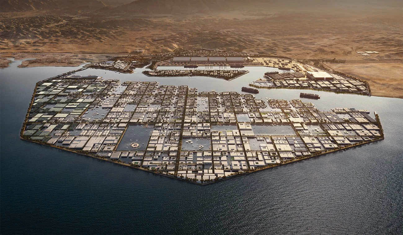Aerial view of a large industrial or commercial complex situated on water with multiple buildings, docks, and a surrounding desert landscape.