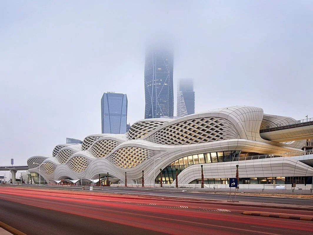Modern architectural building with wavy white exterior and lattice design, situated on a city street with traffic and tall skyscrapers in the background.