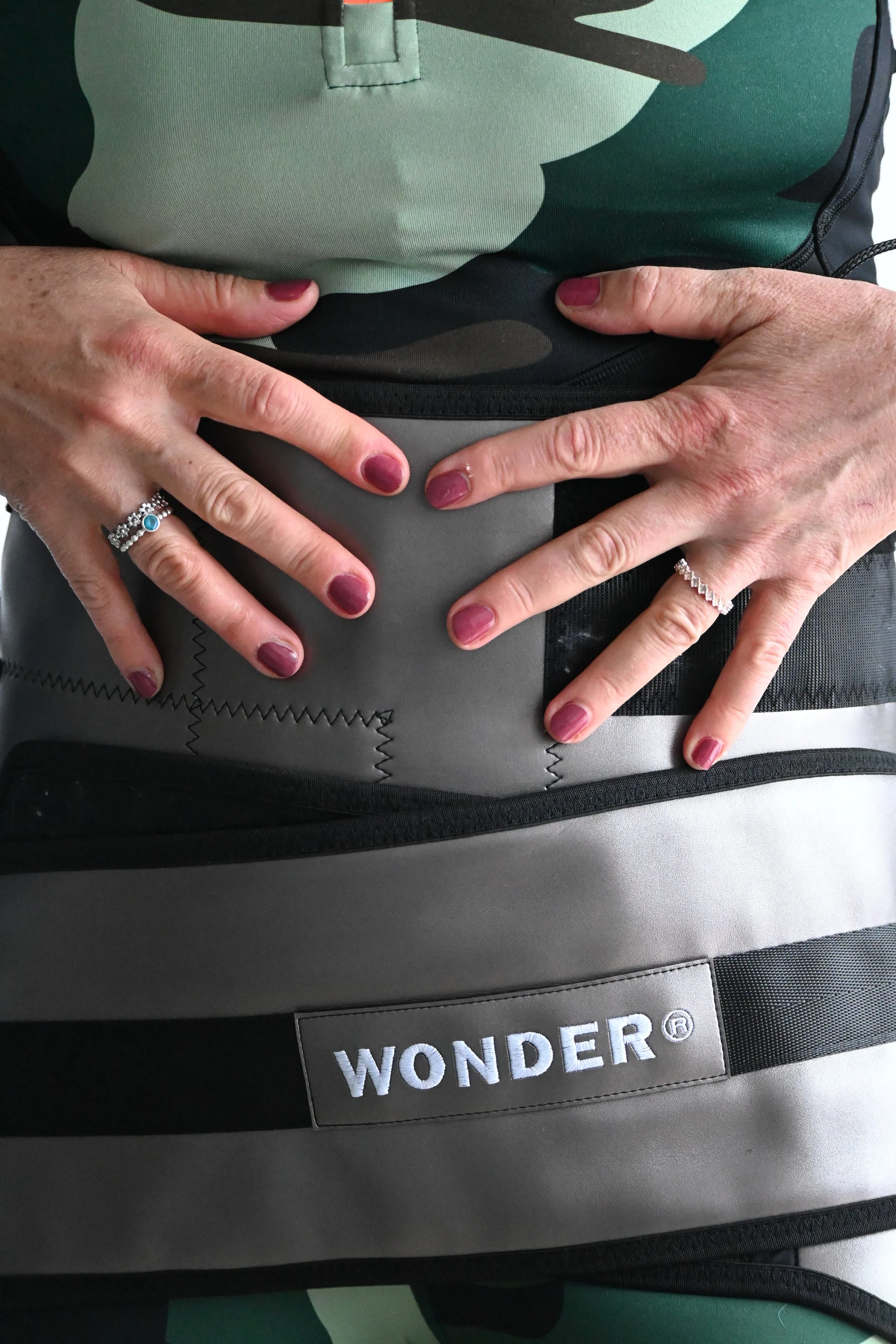 Close-up of hands with rings resting on a gray Wonder backpack with a black strap, showing colorful clothing underneath.