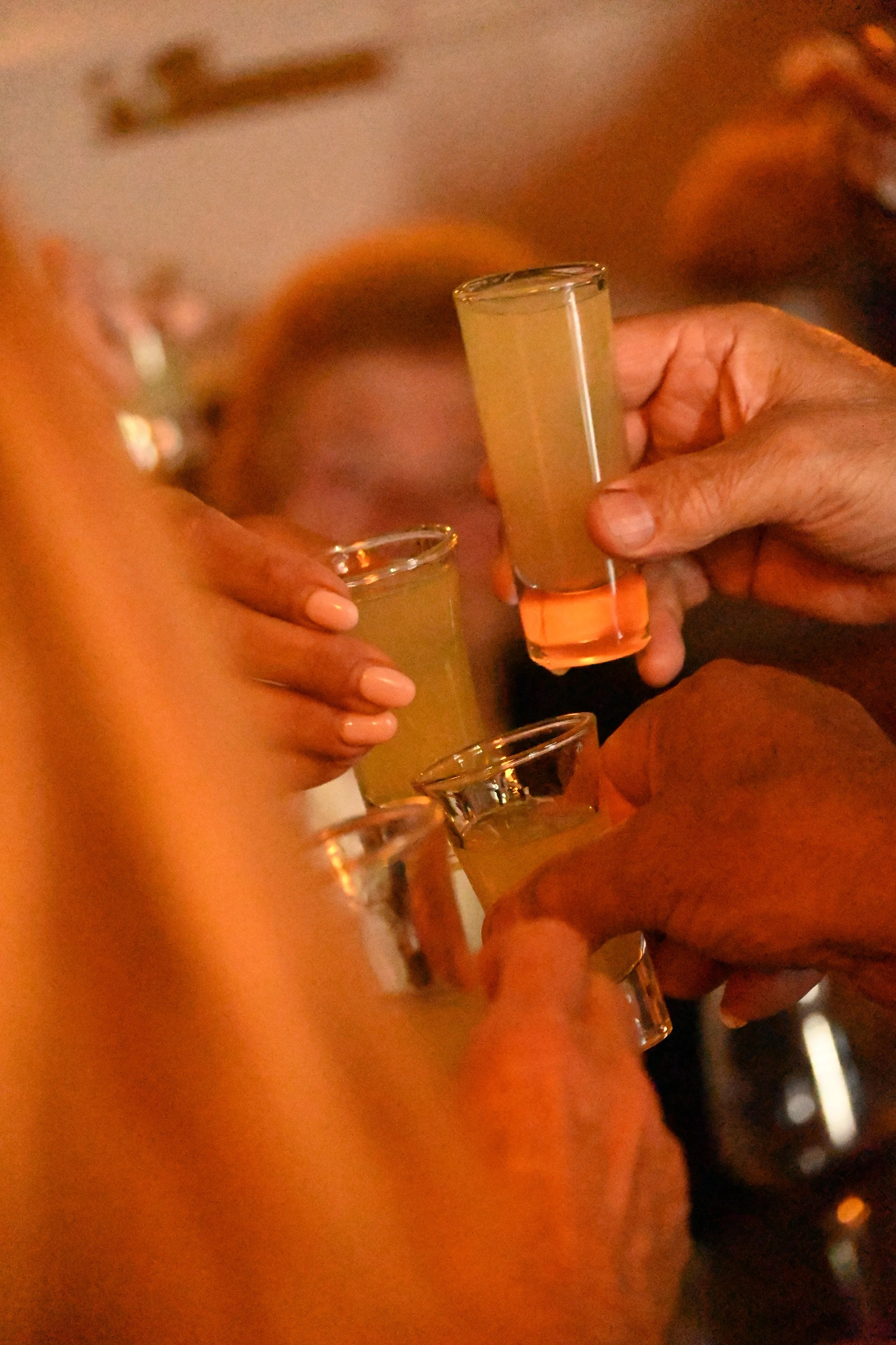 People toasting with shot glasses filled with yellowish liquid in a dimly lit setting.