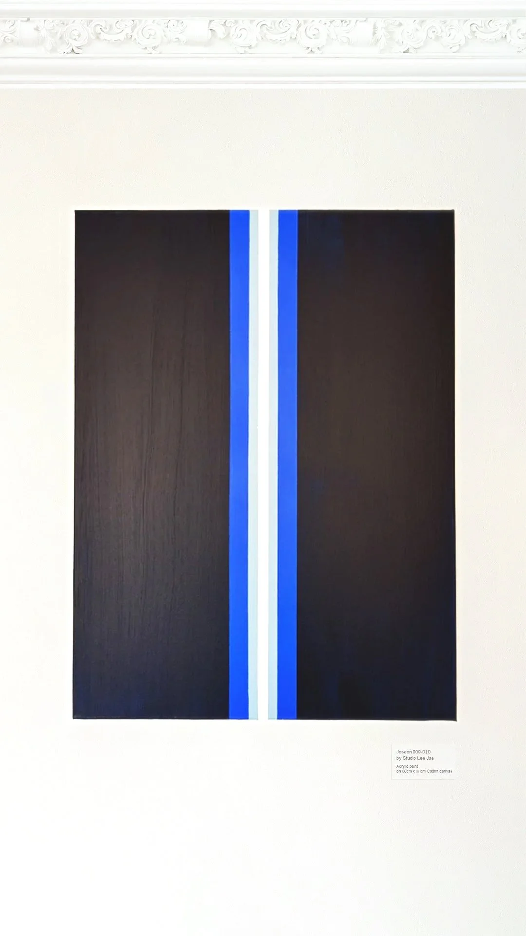 Abstract painting with black background, featuring a vertical blue and white stripe in the center, displayed on a white wall.