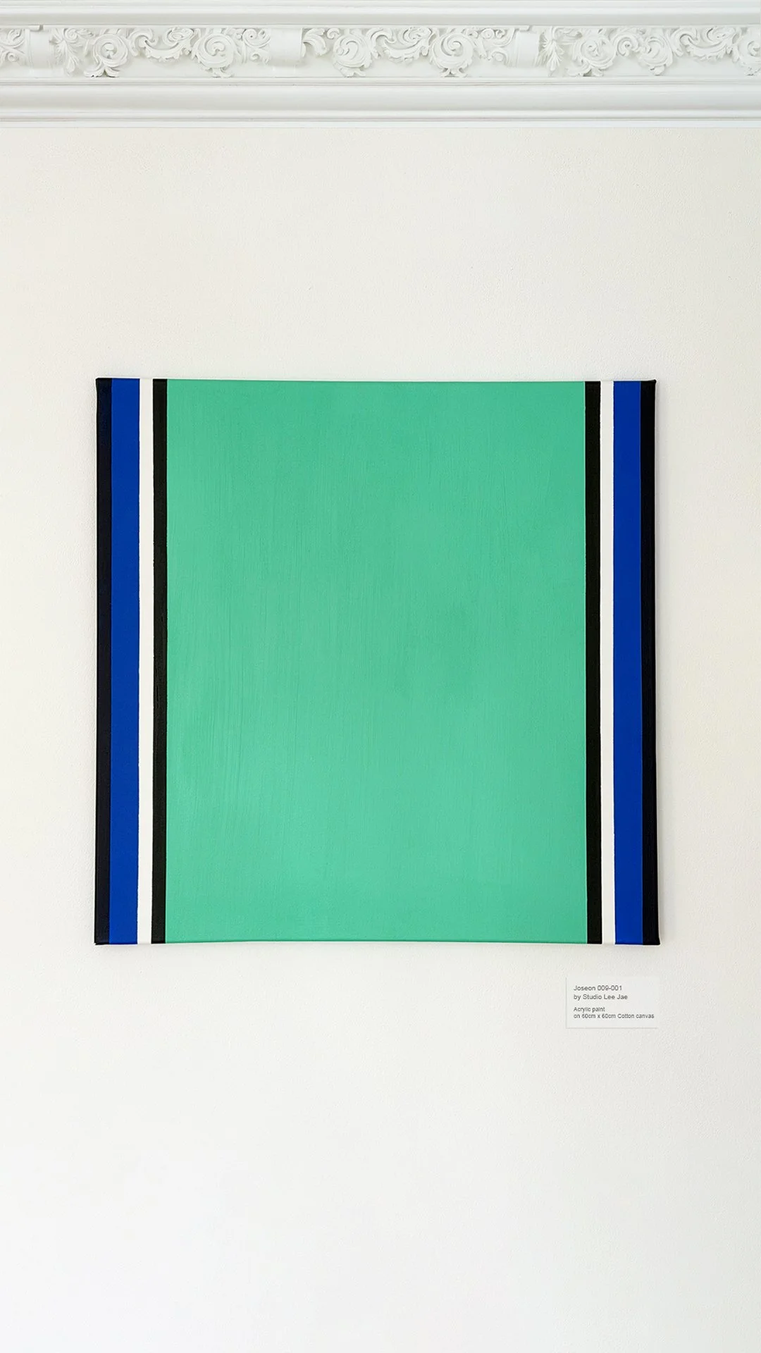 Modern abstract painting with a large green rectangle bordered by vertical stripes of black, white, and blue on a white wall.