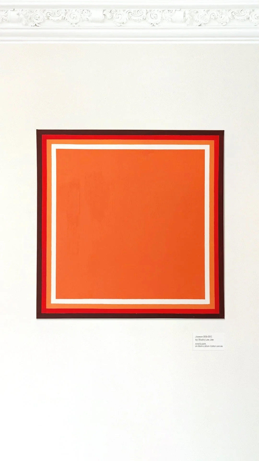 An abstract painting with a large orange square, bordered by white, red, and black lines, on a white wall.