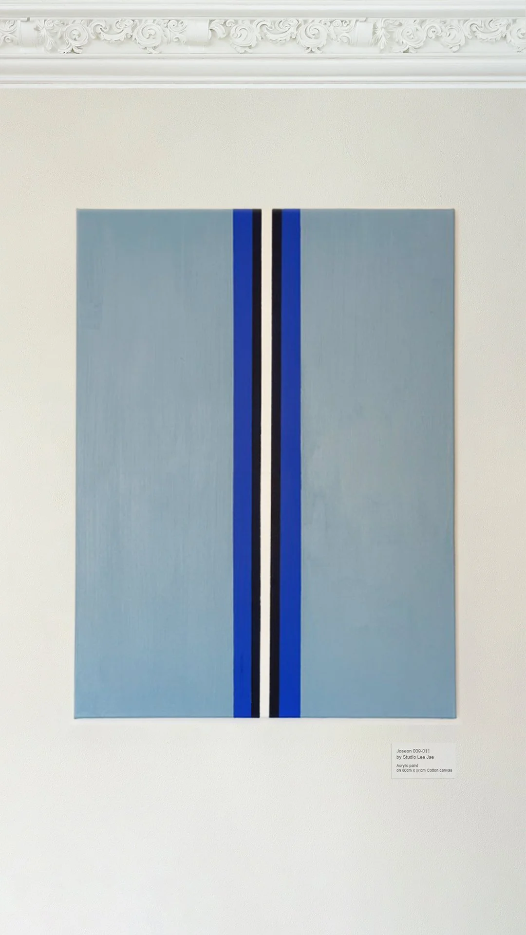 A modern abstract painting with a light gray background, featuring two vertical black lines edged with blue, on a white wall with decorative molding at the top.