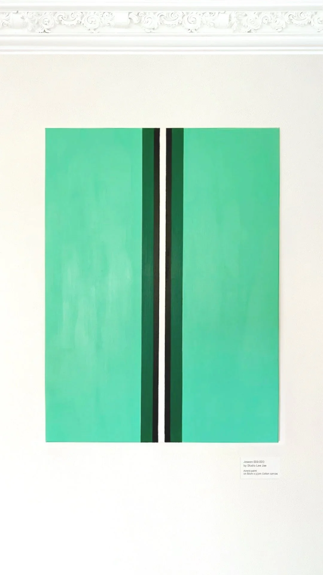 A modern abstract painting with a green background and vertical black and white lines in the center, hung on a white wall with ornate molding at the top.