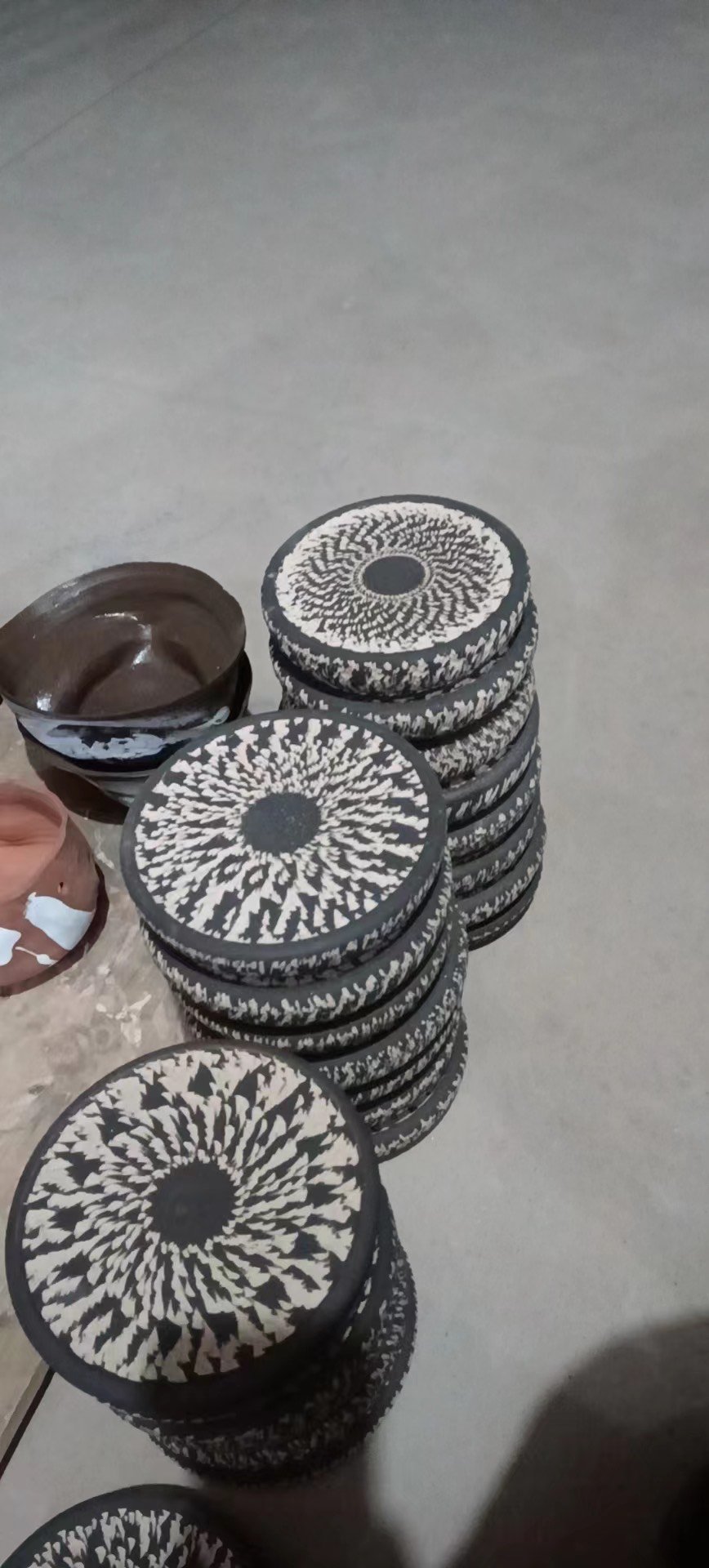 Stack of black and white patterned coasters or discs placed on a surface with a bowl of brown substance nearby.