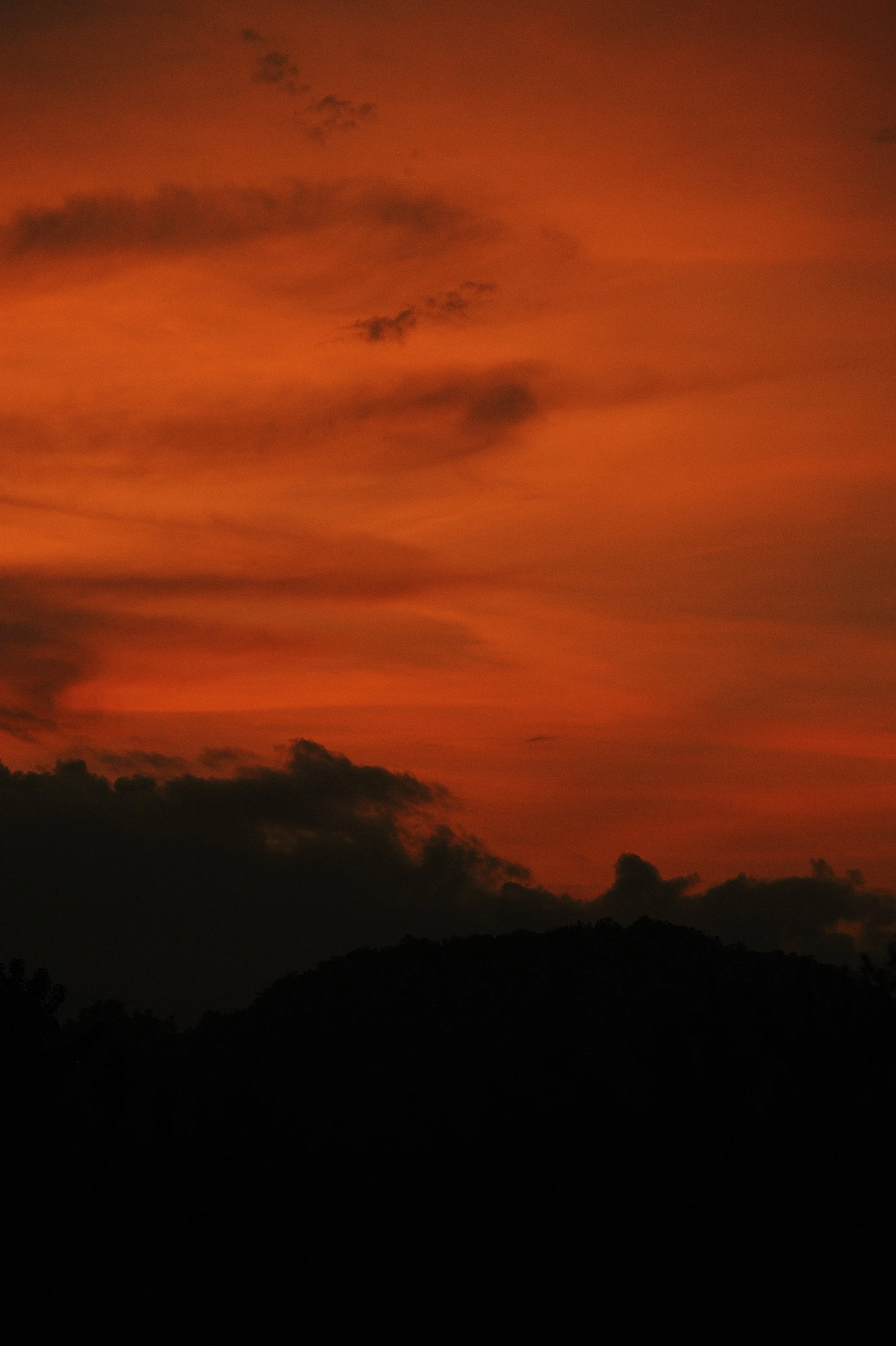 Dark mountain silhouette against a vibrant orange and pink sunset sky with scattered clouds.