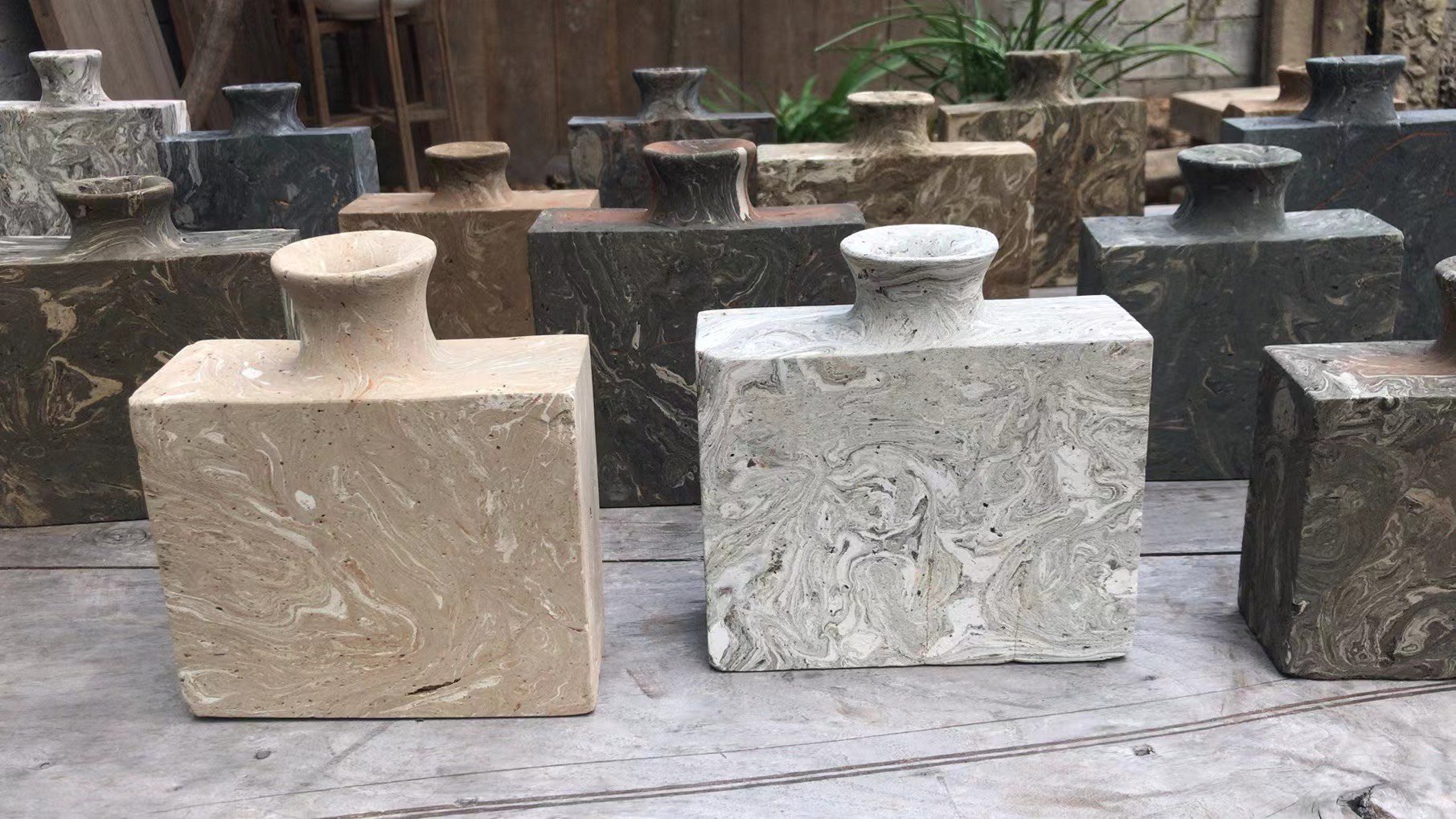 Collection of marble vases in various colors and textures arranged on a wooden surface outdoors.