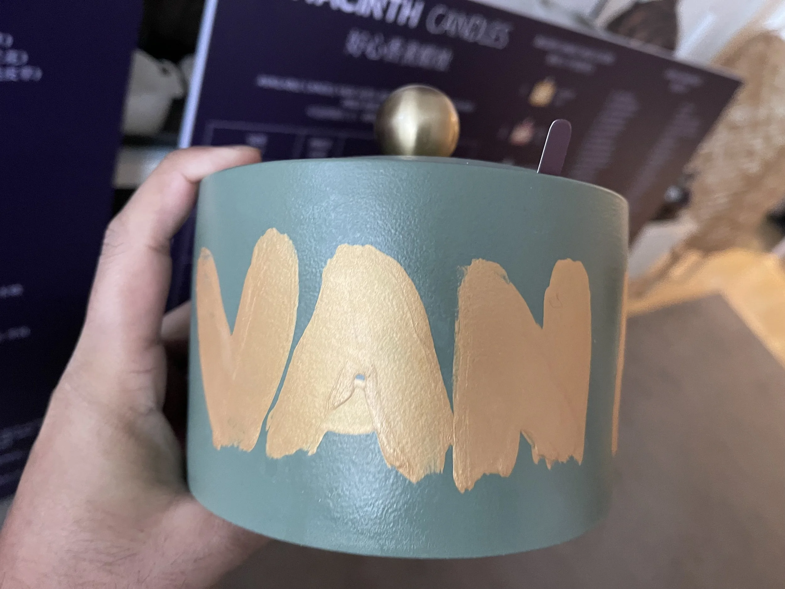 A hand holding a teal ceramic mug with the word 'WARM' painted in large, gold letters.