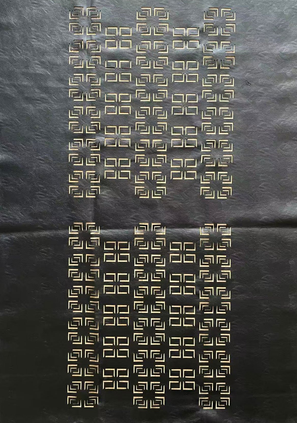 A sheet of black paper with intricate cut-out geometric patterns in a grid, forming a design with repeated square motifs.