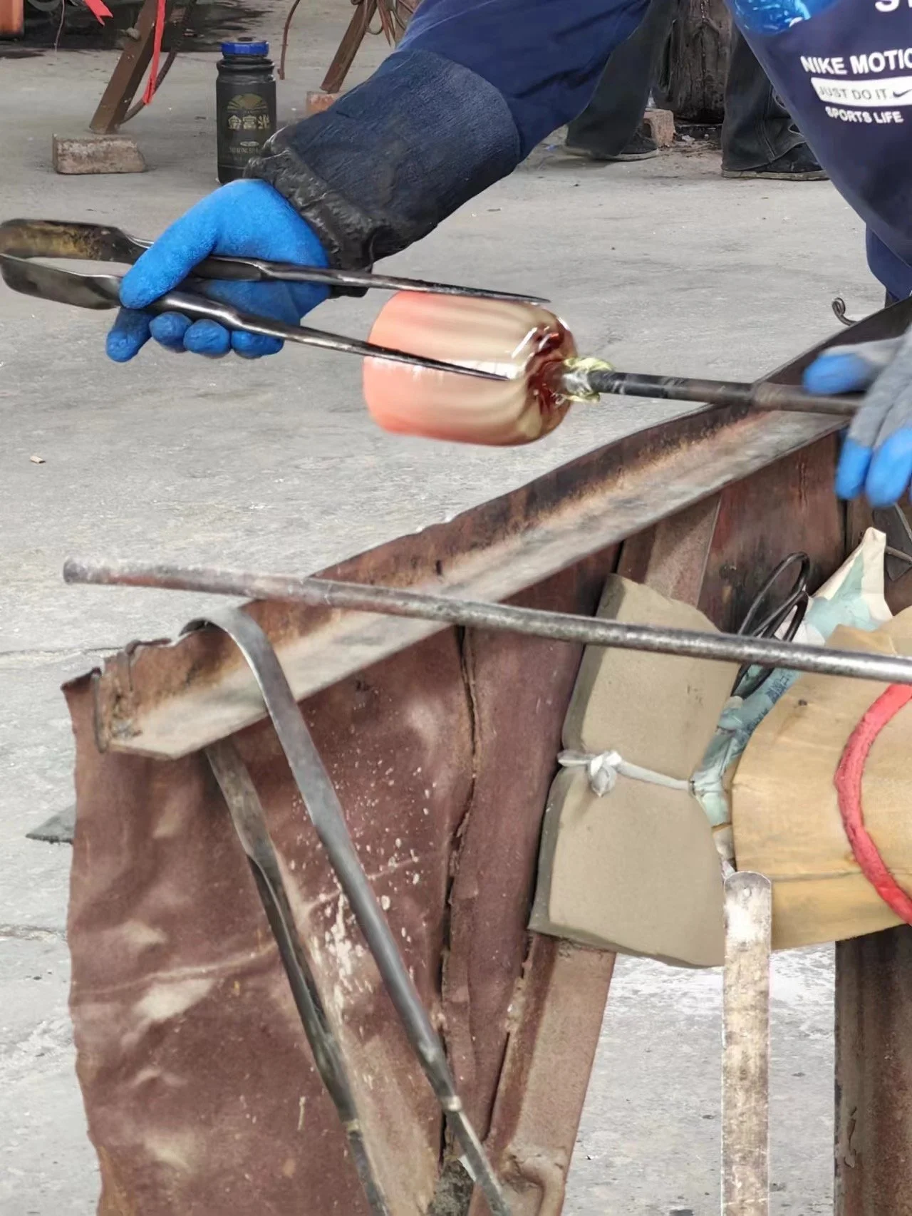 A glassblower in gloves shaping molten glass on a metal rod at a glassblowing workshop.