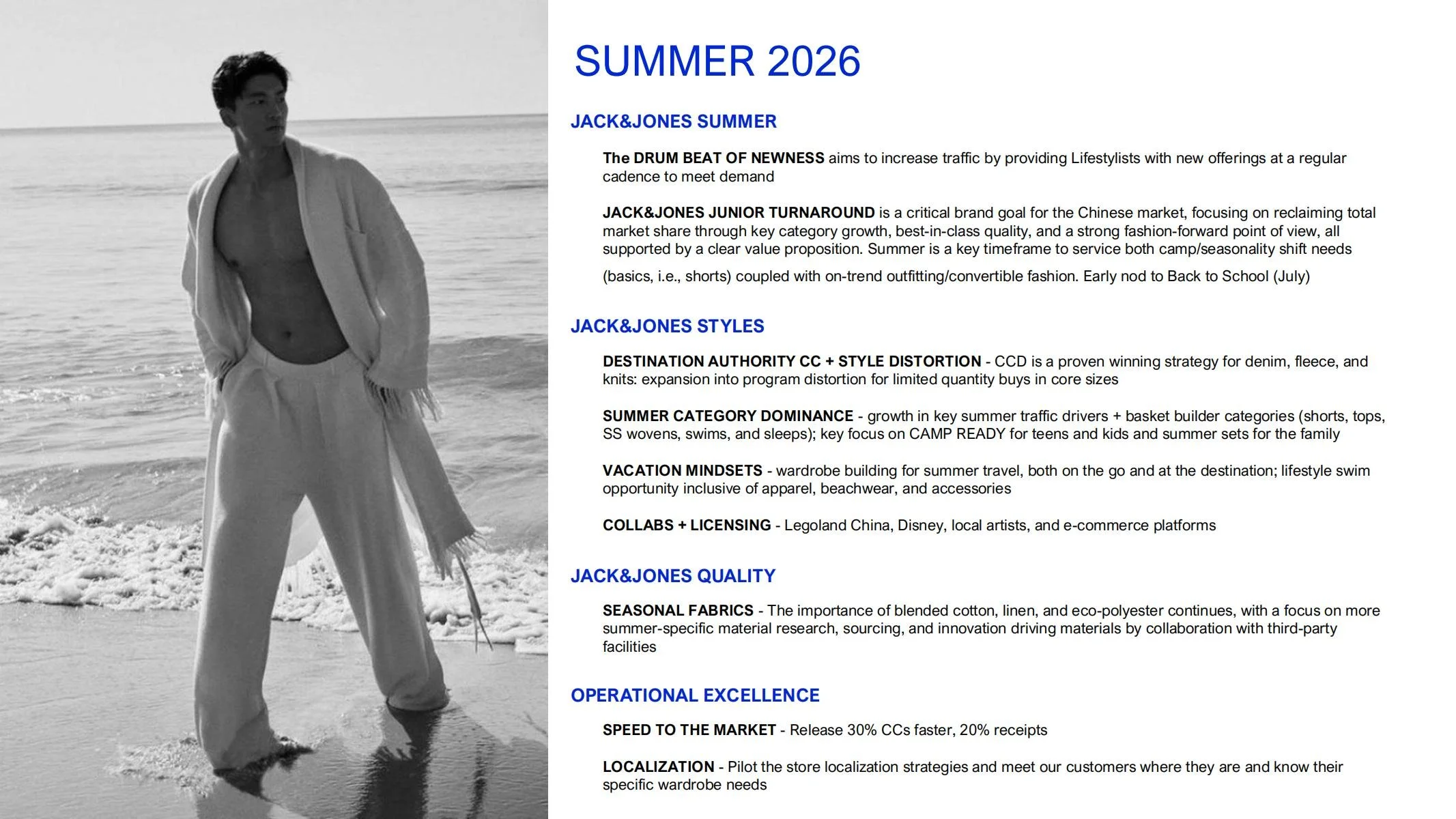 A black-and-white image of a man standing on a beach near the water, wearing a light-colored open shirt and matching pants, with a towel draped over his shoulders, looking off into the distance.