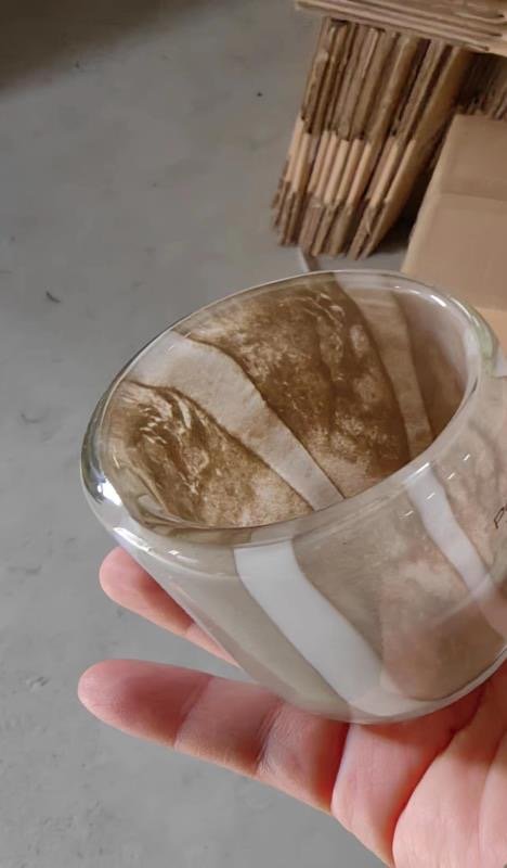Hand holding a small glass bowl with coffee art or a coffee swirl design.