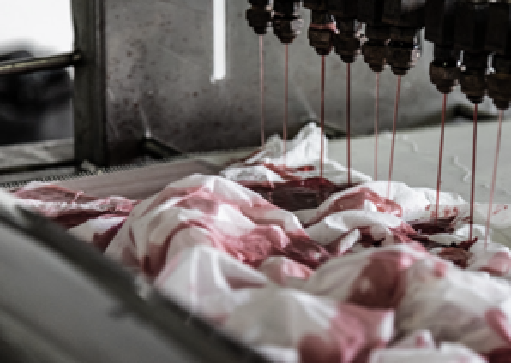Industrial machine pouring blood onto raw meat in a meat processing plant.