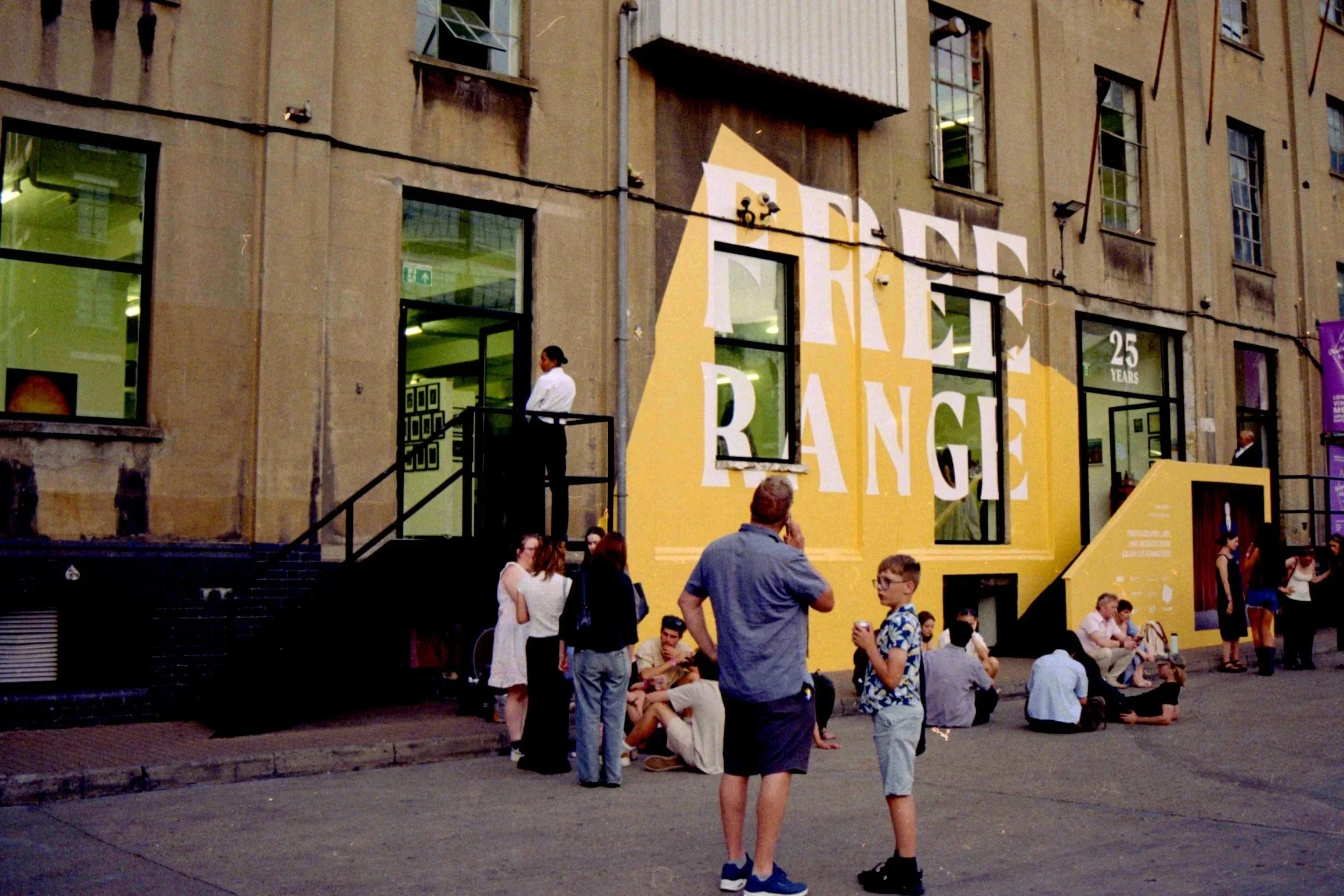 People gathering outside a building with yellow and white signage that reads 'FREE RANGE' and '25 YEARS'.