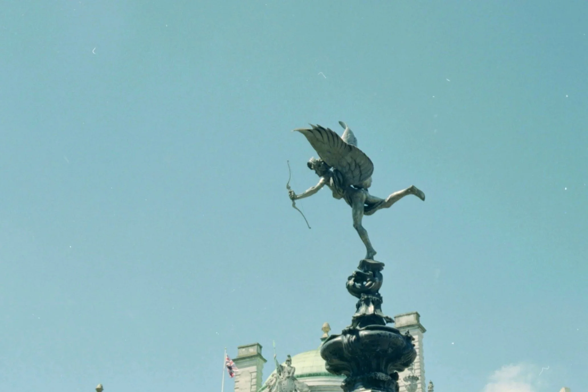 A statue of a winged figure holding a bow and arrow atop a building, with a clear blue sky in the background.