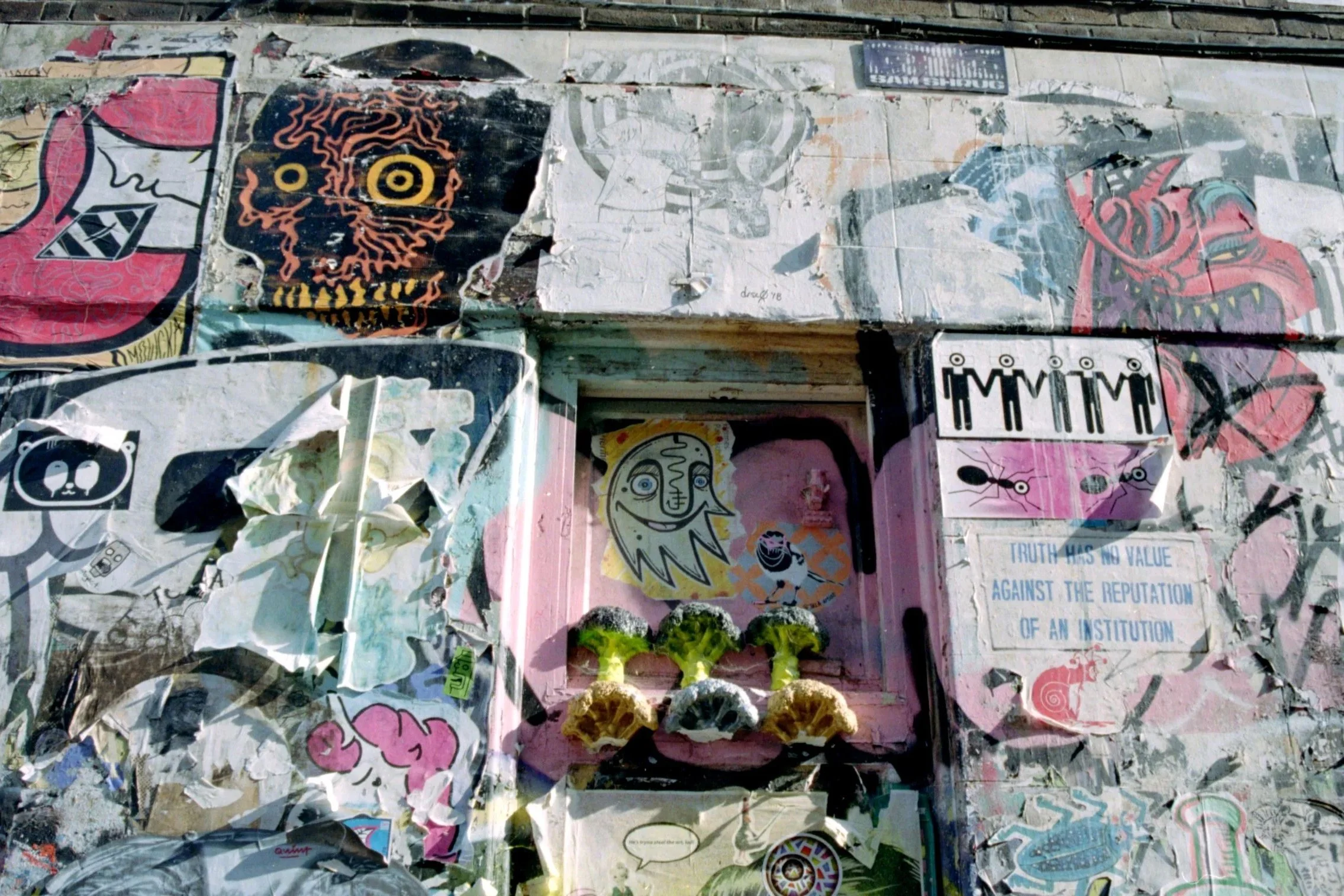 A collection of torn and overlapping posters and stickers on a wall, featuring various artwork, text, and illustrations.