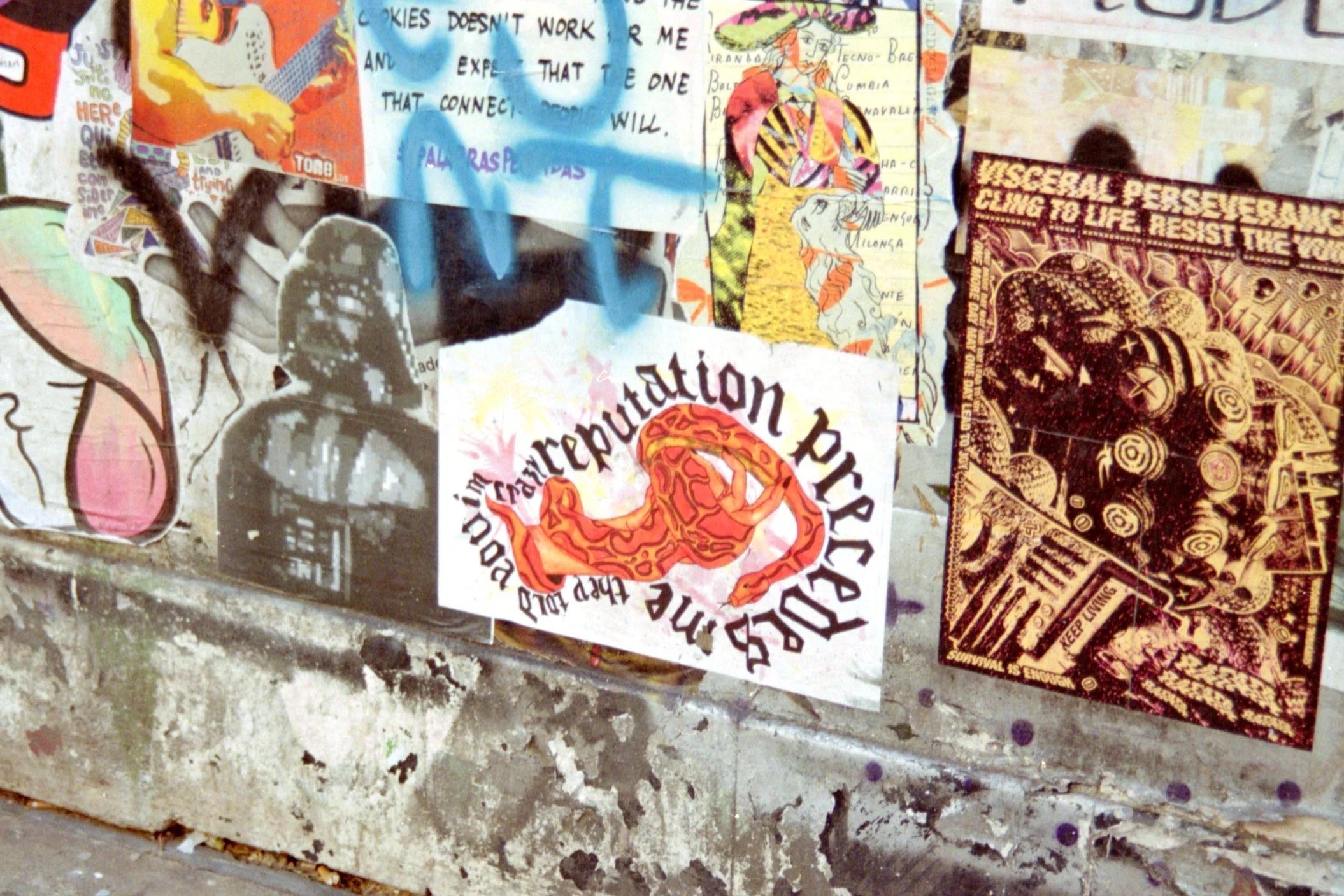 A collage of various stickers, posters, and artwork on a wall, including colorful drawings, text snippets, and protest signs, with some images of people and symbols.