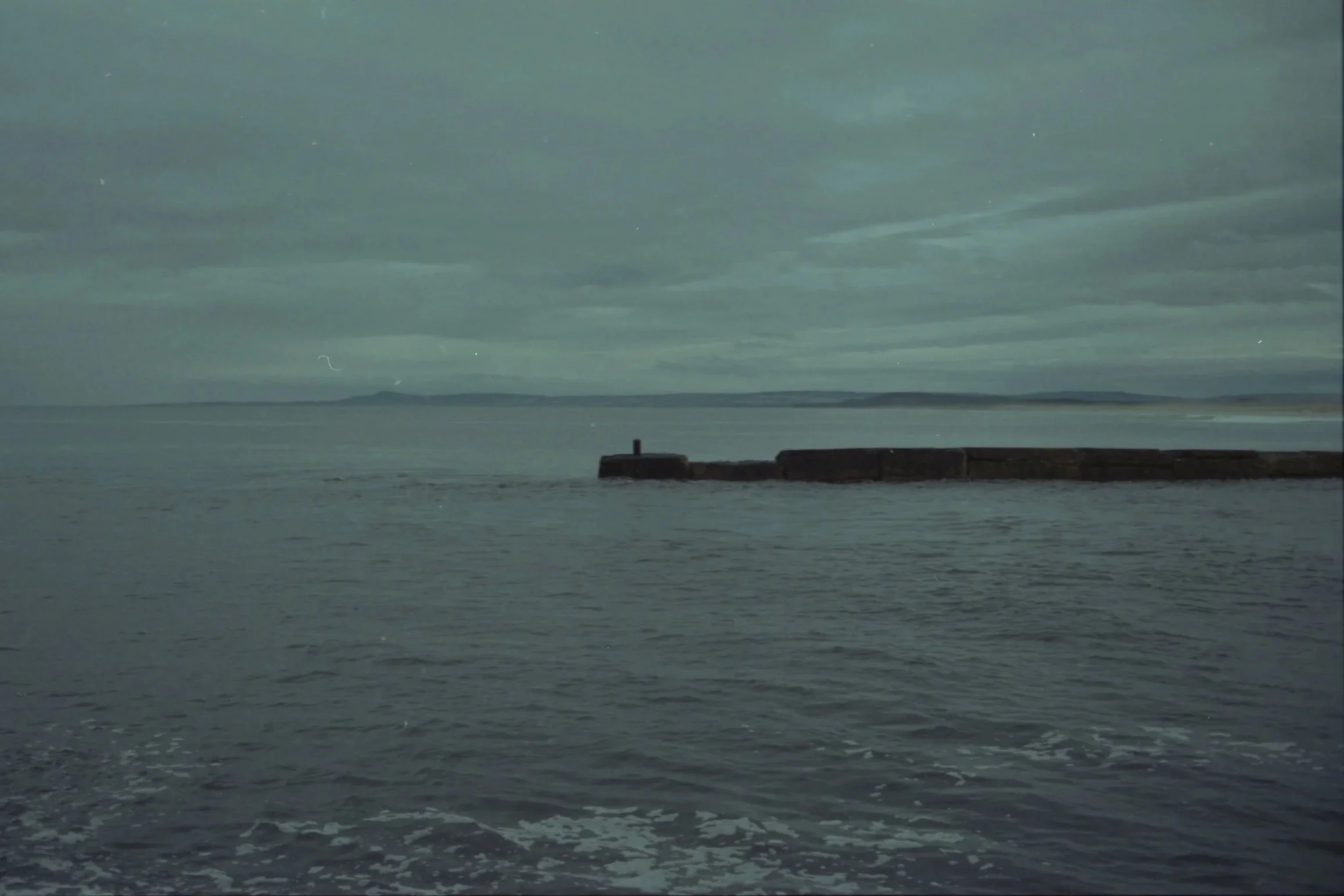 A body of water with a pier extending into it and land in the distance under a cloudy sky.