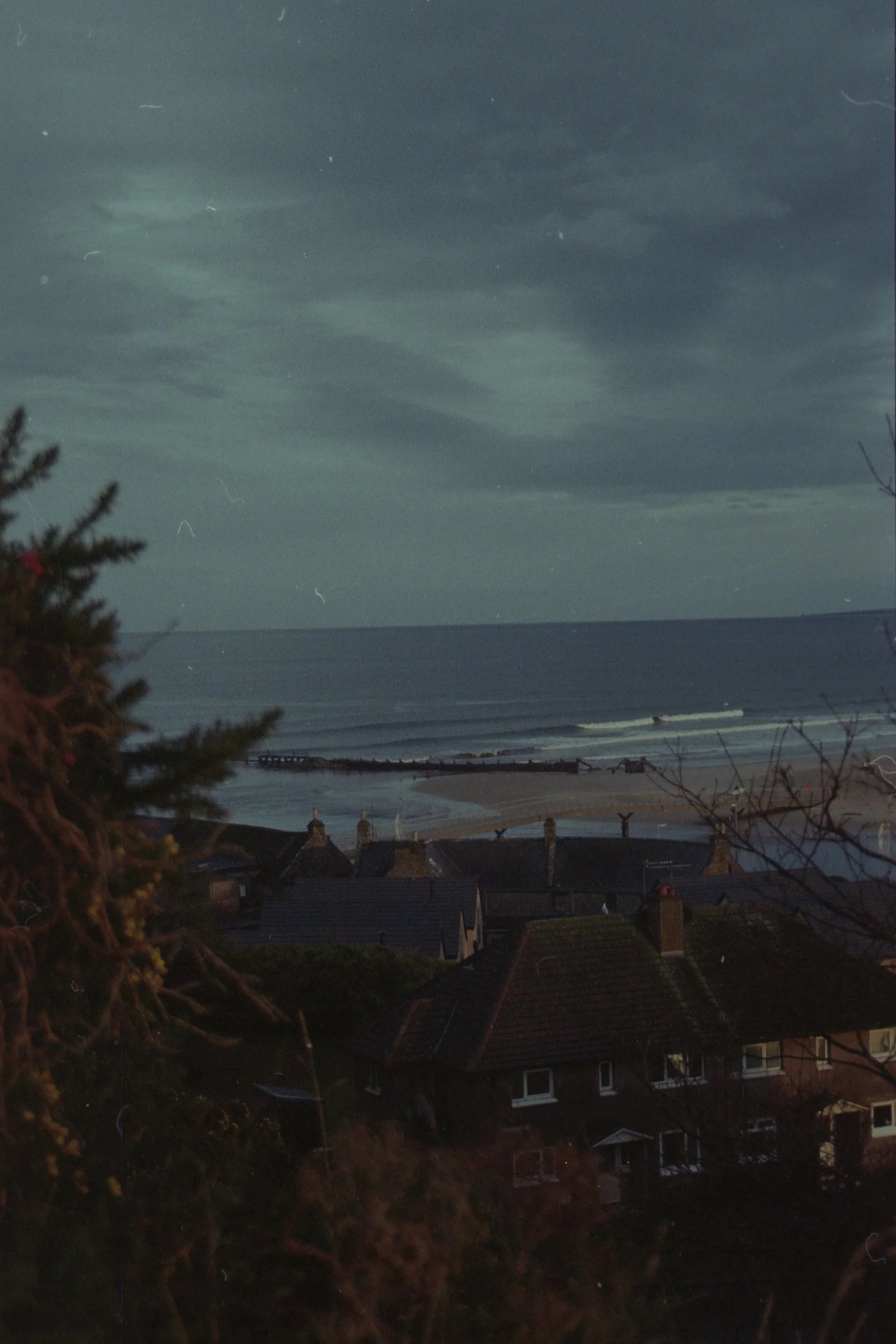 Nighttime view of a coastal village with houses, a beach, and the ocean, under a mostly cloudy sky.