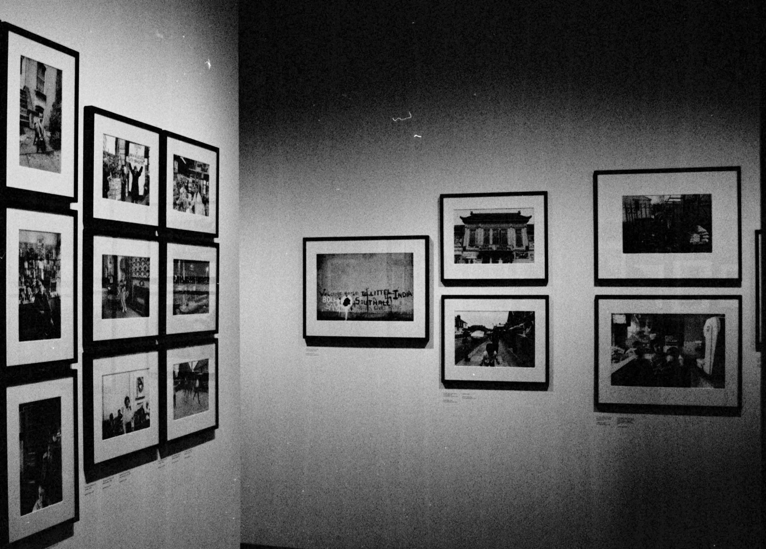 Black and white wall with framed photographs or artwork in an exhibition setting.