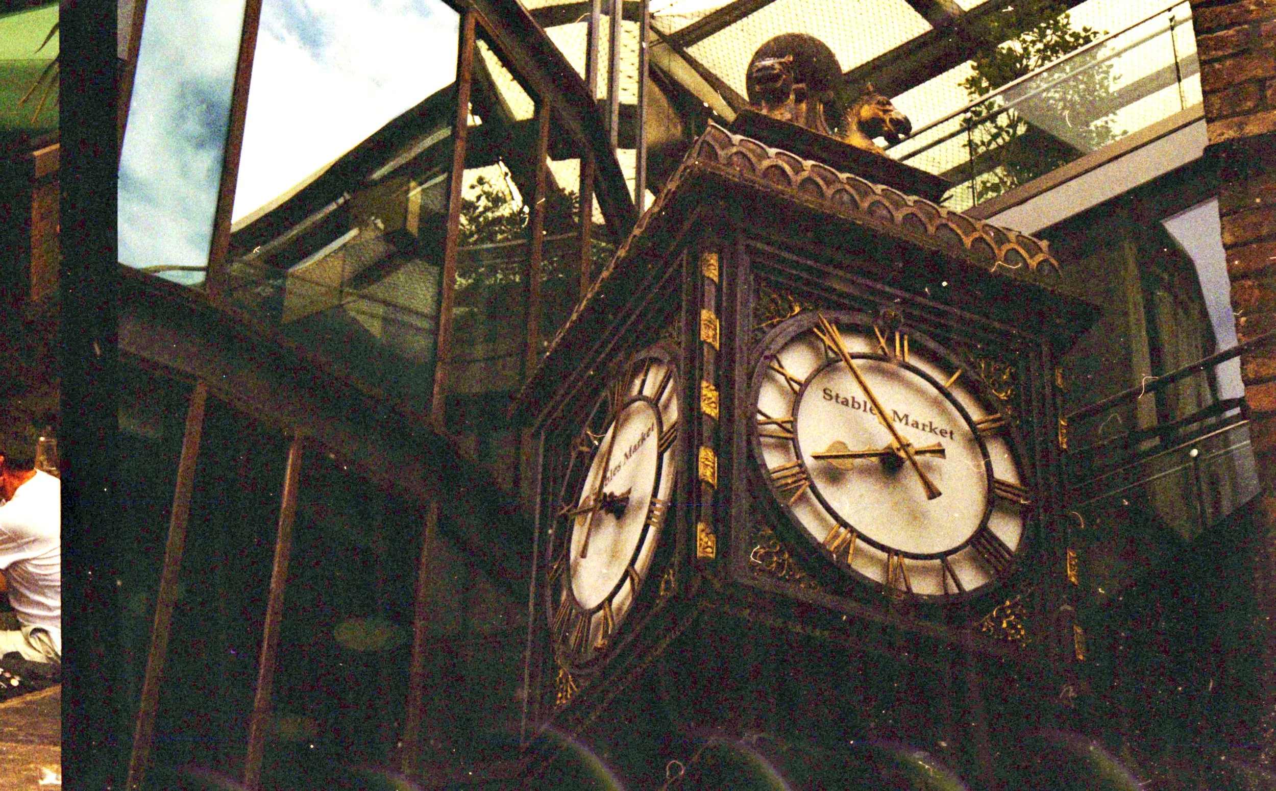 Close-up of a vintage clock with roman numerals, part of a larger clock display, with visible clock hands and the text 'Stable Market' on the dial, taken from a low angle.