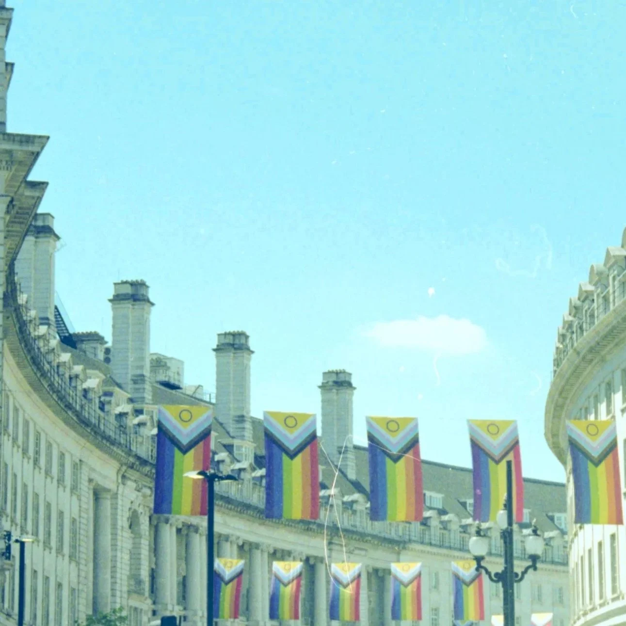 Decorated street with rainbow flags and ornate buildings under a clear blue sky.