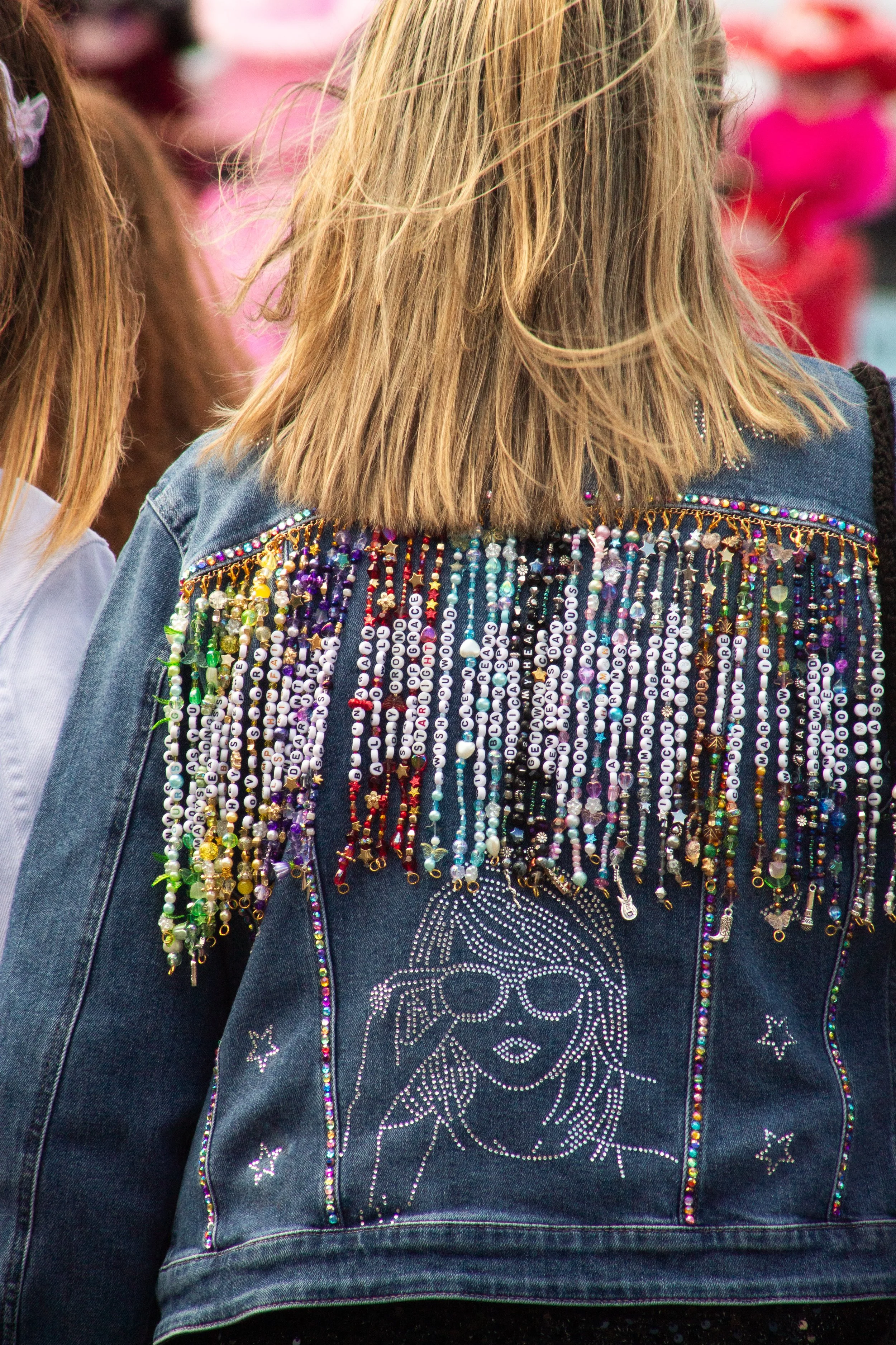 Back of a person wearing a denim jacket decorated with colorful beads and rhinestones, featuring a skull design on the back.
